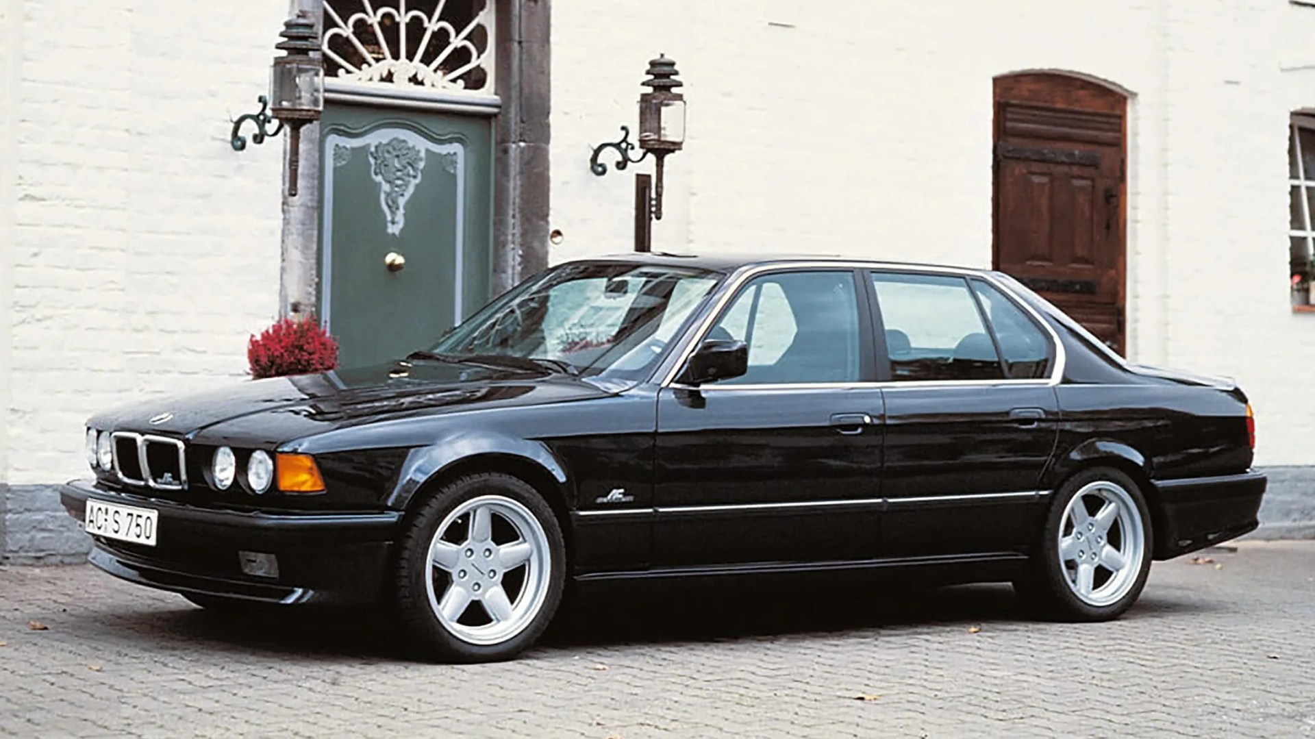 Black classic BMW sedan with silver five-spoke wheels parked on a cobblestone street.