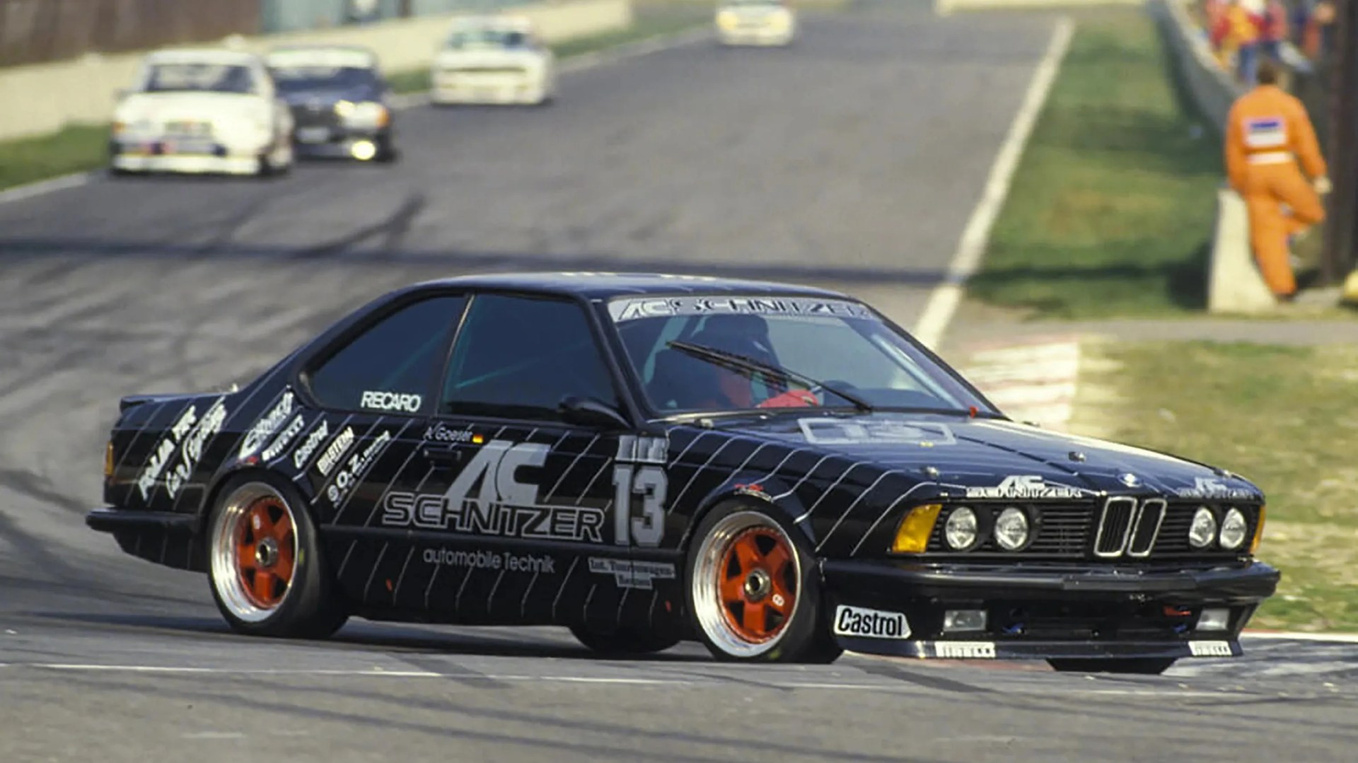 Black AC Schnitzer race car with orange wheels and number 13 on a racetrack.