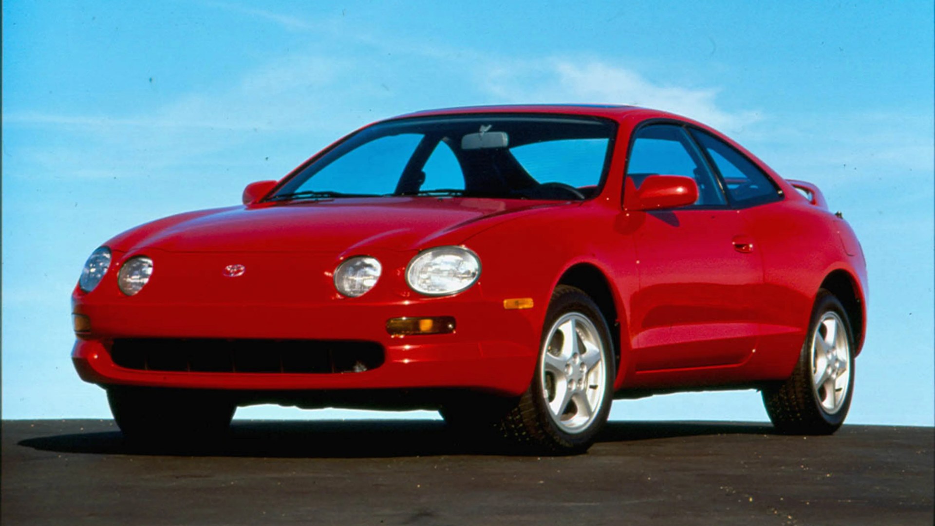 Red two-door sports coupe with round headlights and silver alloy wheels on asphalt.
