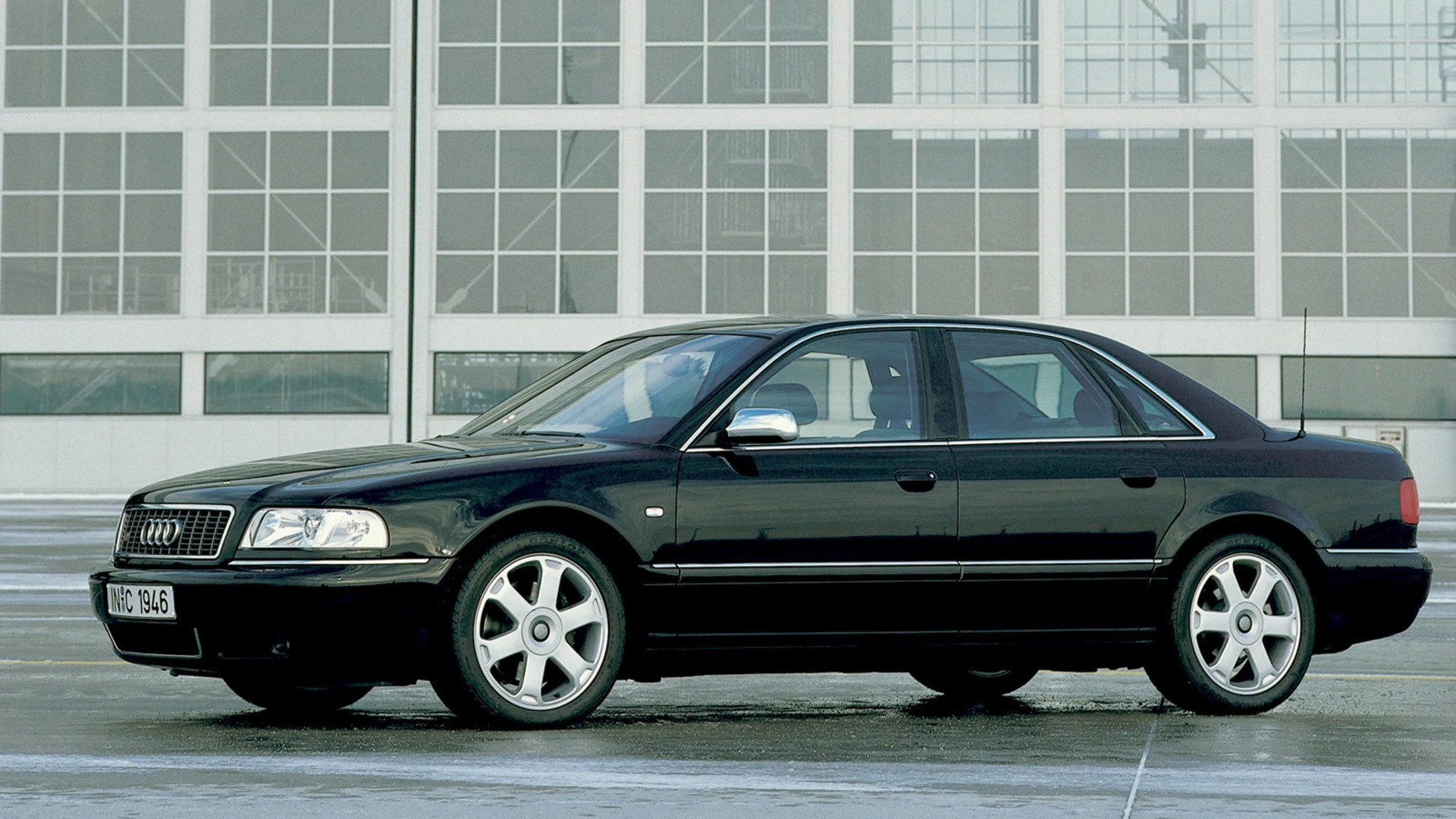 Black Audi sedan with silver alloy wheels parked in front of a large windowed building.