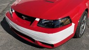 Front of a red Ford Mustang with white tape covering the lower bumper area, parked on asphalt.