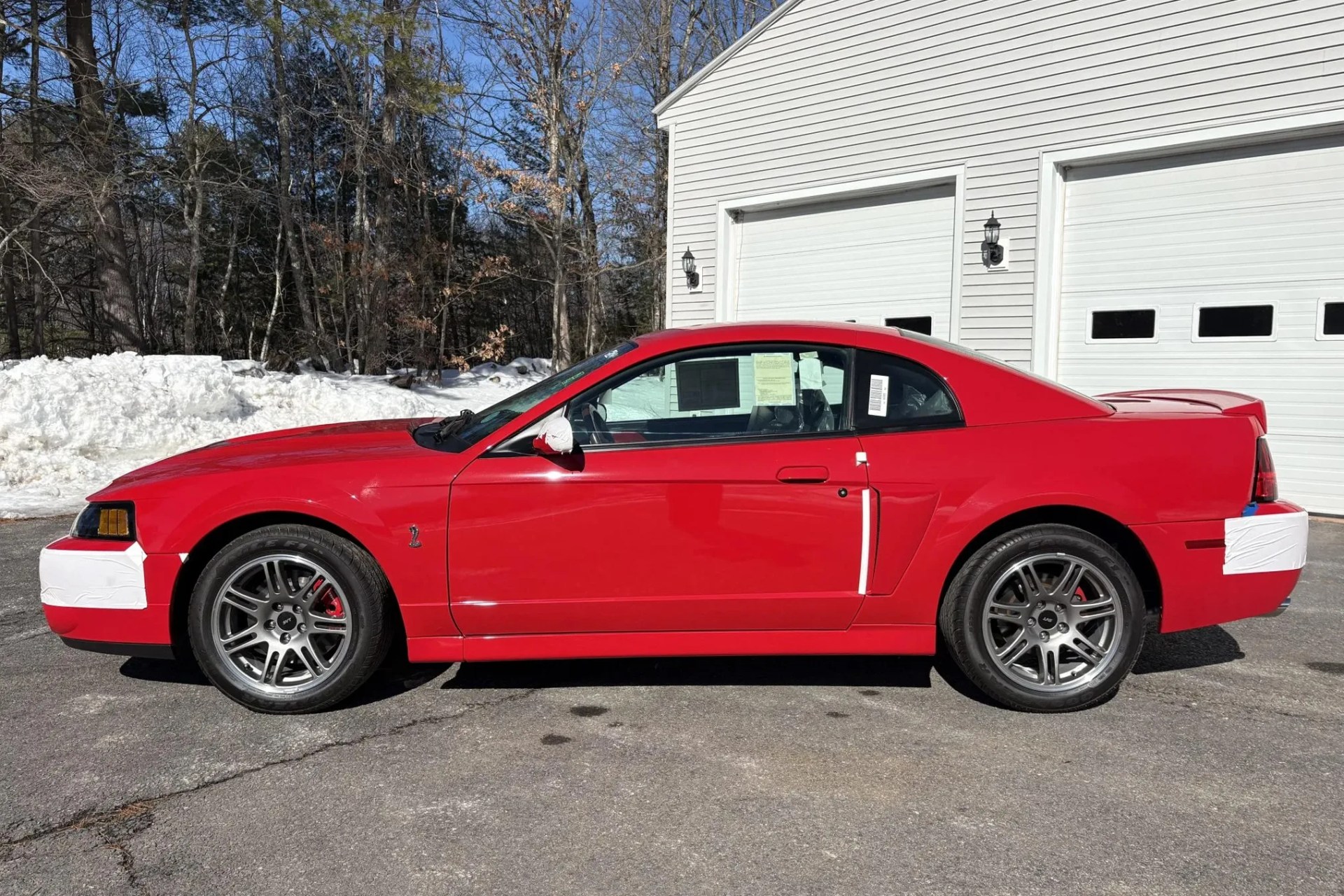 Red Ford Mustang Cobra with silver wheels parked on driveway in front of white garage doors.