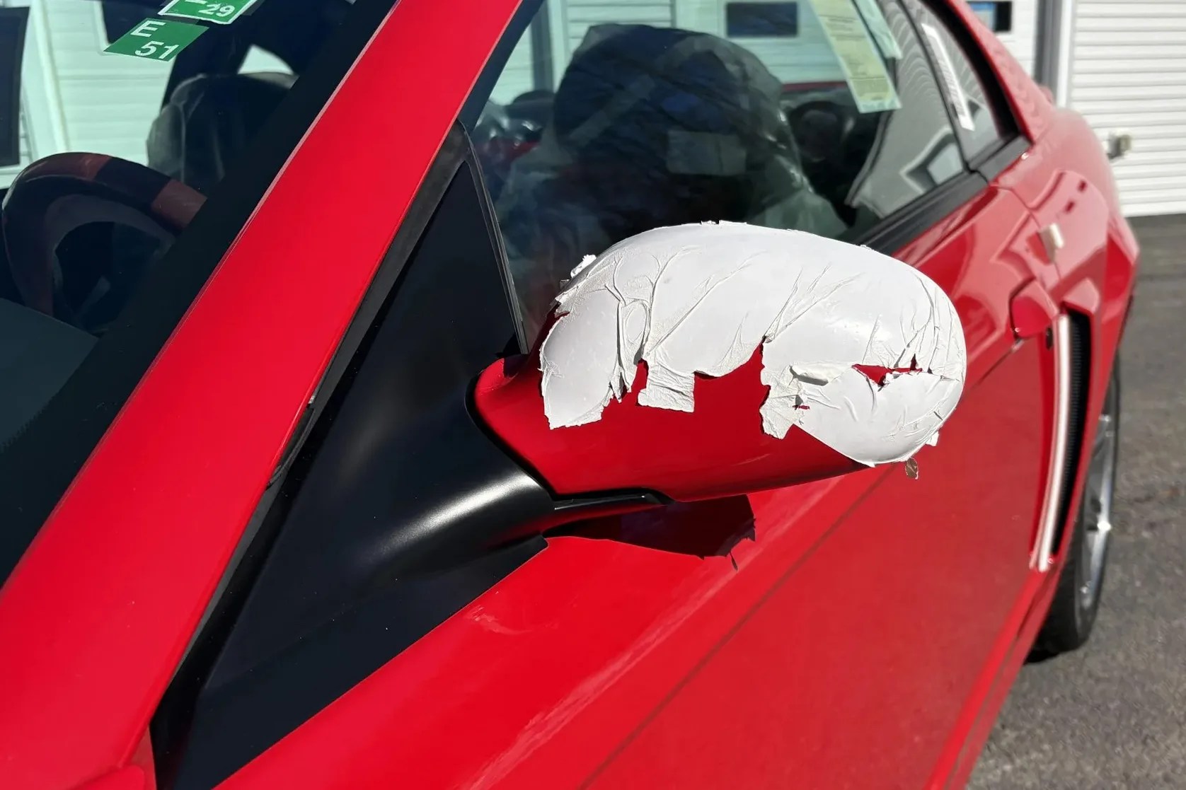Red car side mirror with peeling white paint on the outer shell.