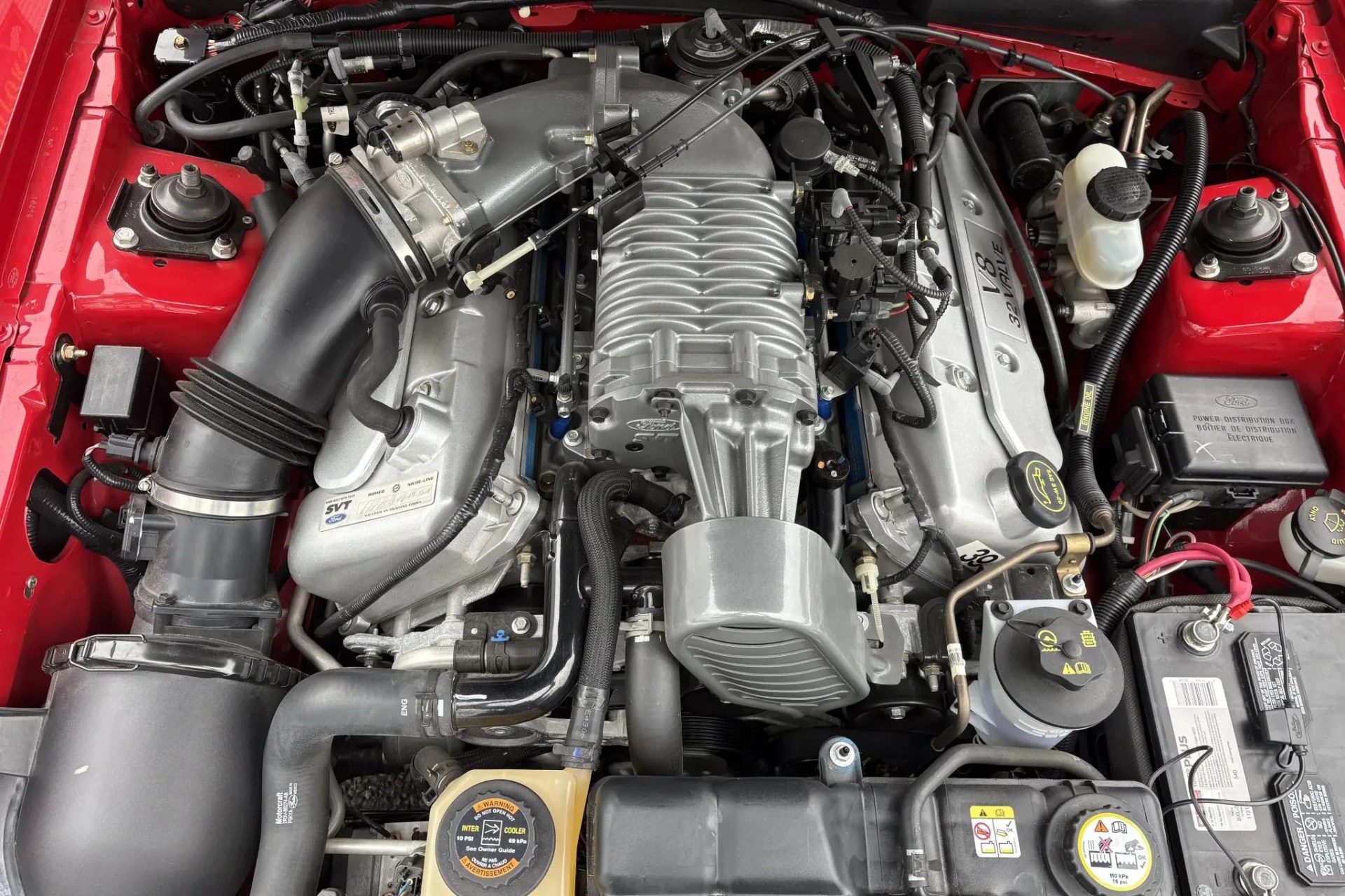 Silver V8 32-valve engine with supercharger and black air intake hose in a red engine bay.