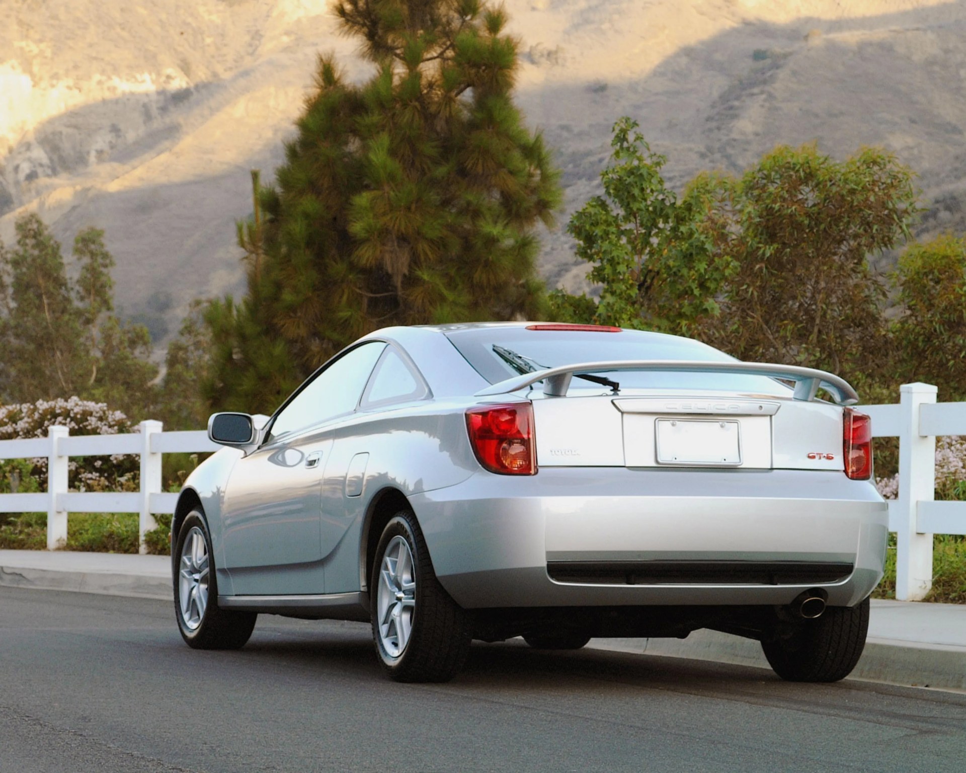 Silver Toyota Celica GT-S coupe parked on a road with mountains and trees in the background.