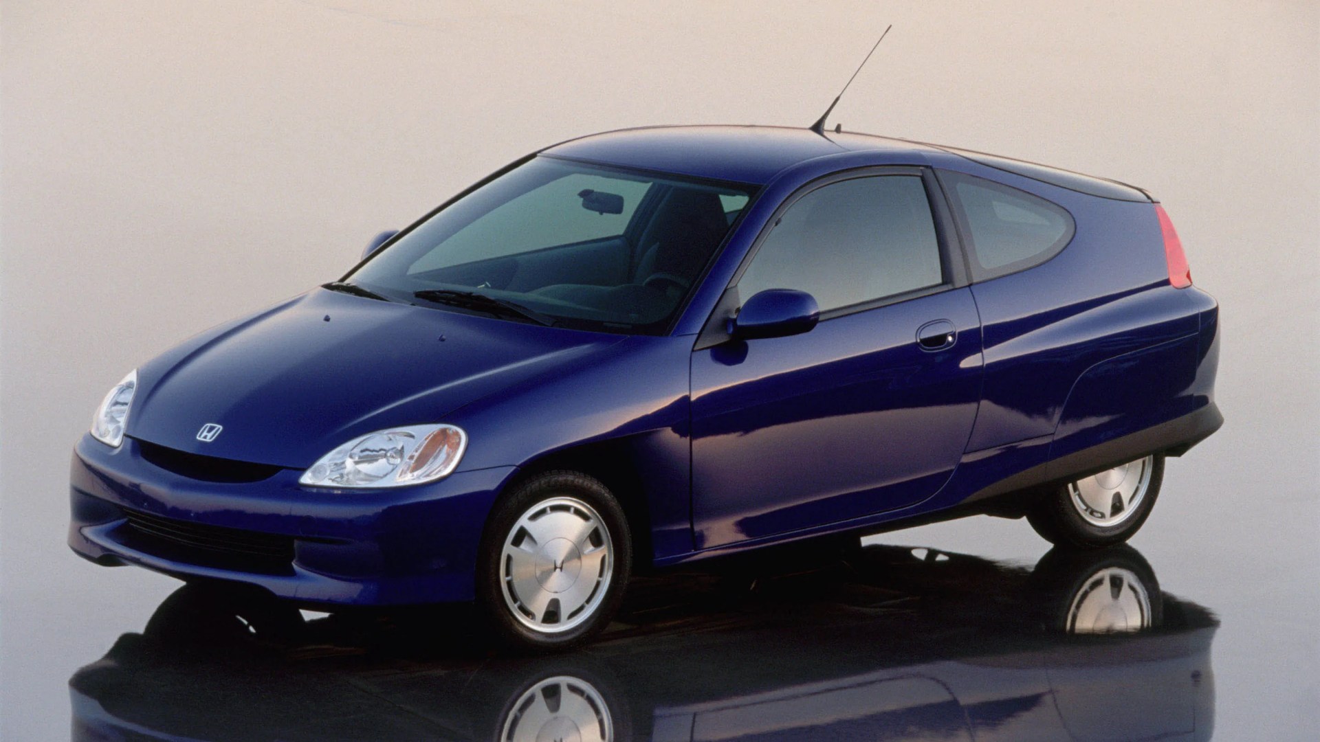 Blue three-wheeled Honda Insight hatchback with aerodynamic design on reflective surface.