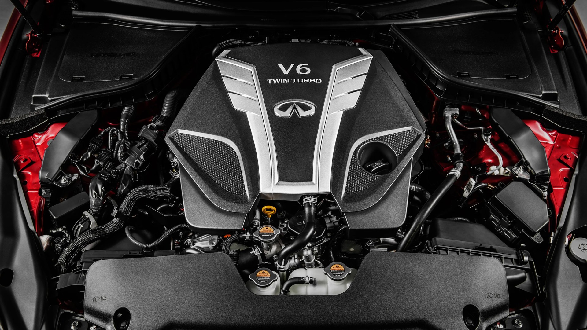 V6 twin turbo engine with Infiniti logo under a car hood with red body panels.