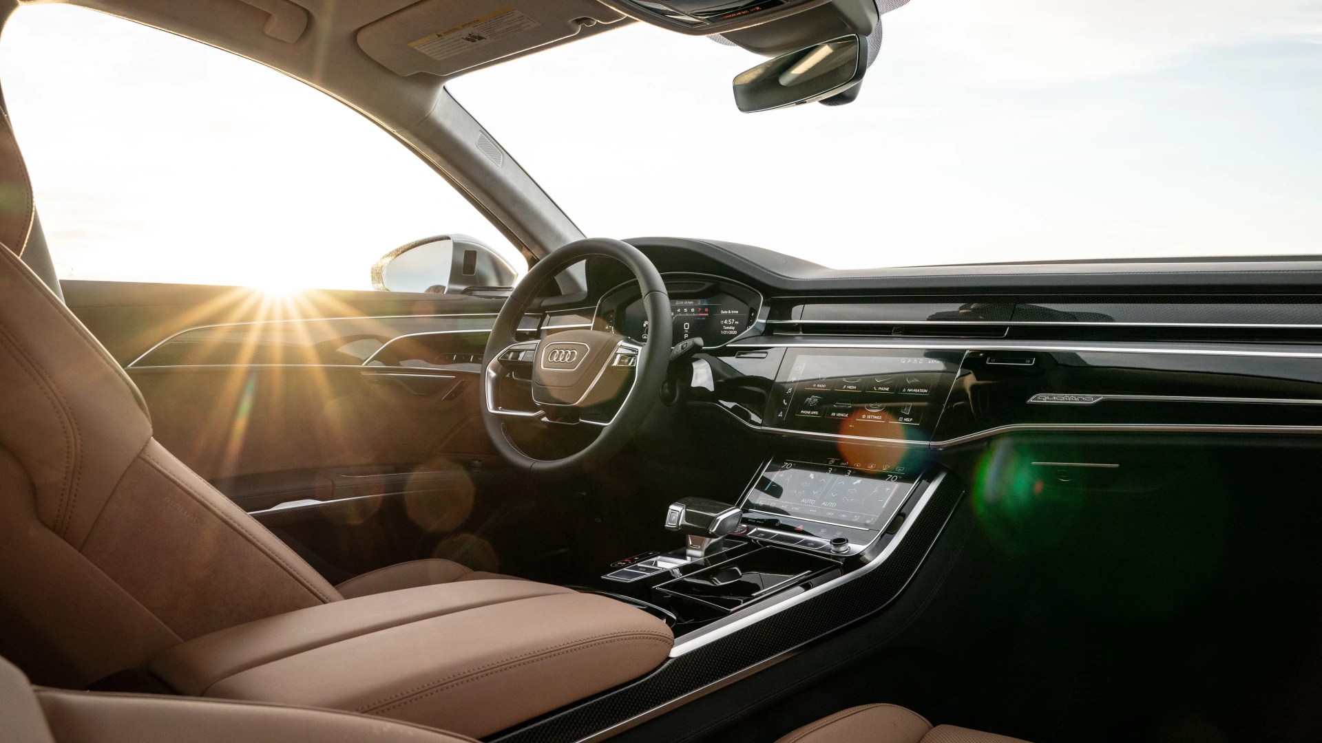 Audi car interior with tan leather seats, digital dashboard, and dual touchscreen center console at sunset.