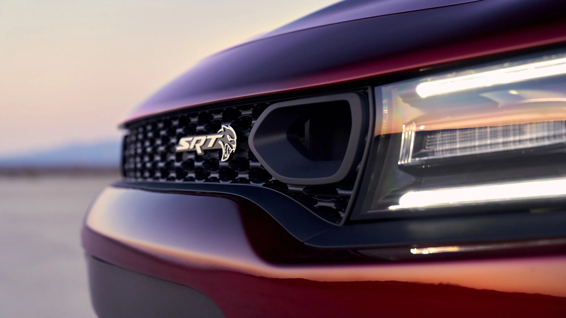 Close-up of a red car's front grille with an SRT Hellcat logo and a modern LED headlight.