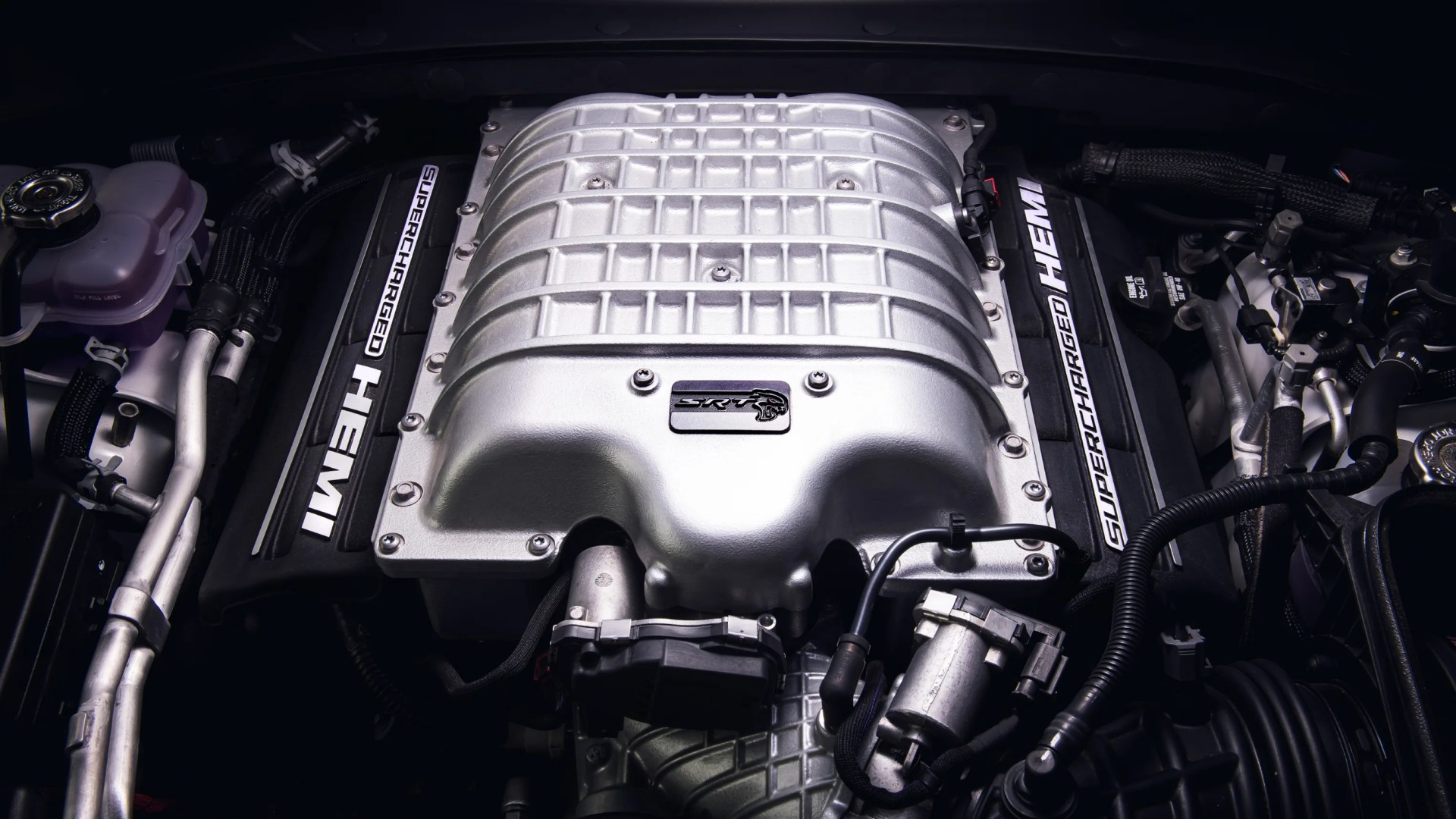 Silver supercharged HEMI engine with "SRT" badge and black components surrounding it.