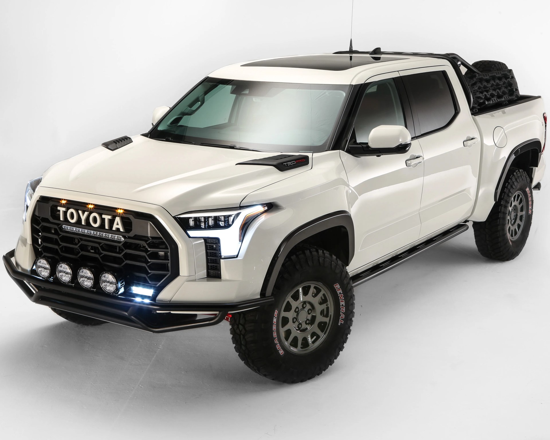 White Toyota TRD Pro pickup truck with black grille, off-road tires, and roof sunroof in a studio setting.