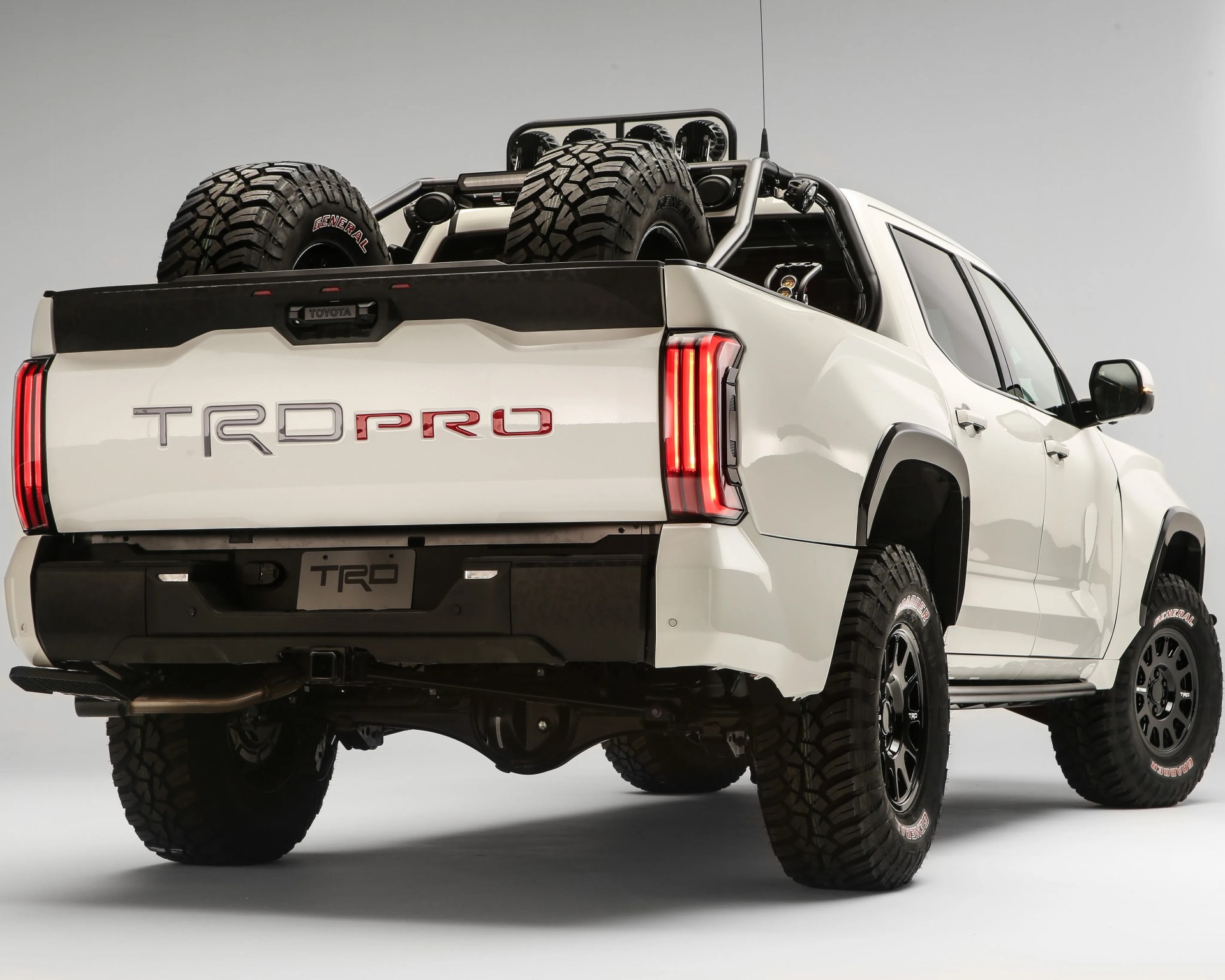 White Toyota TRD Pro pickup truck with off-road tires and two spare tires mounted in the bed.