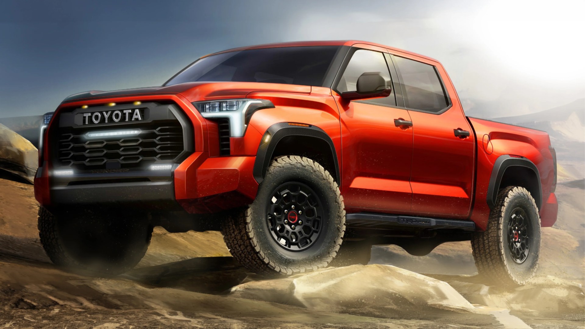 Red Toyota pickup truck with black grille and off-road tires on rocky terrain.