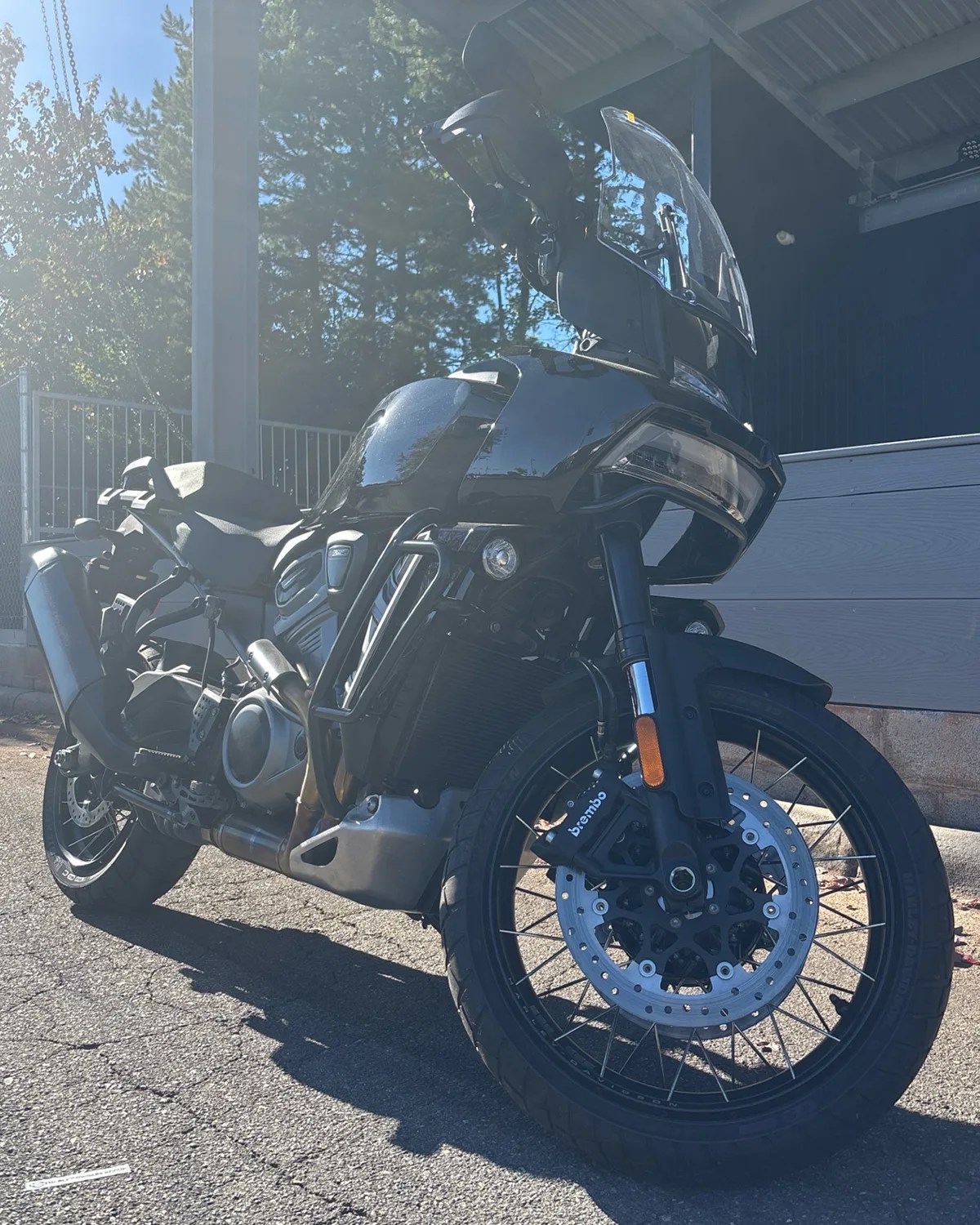 Black adventure motorcycle with a tall windshield and Brembo front disc brakes parked on asphalt.