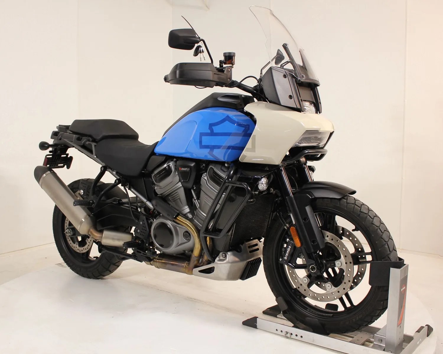 Blue and white adventure motorcycle with black frame and exhaust, mounted on a front wheel stand.