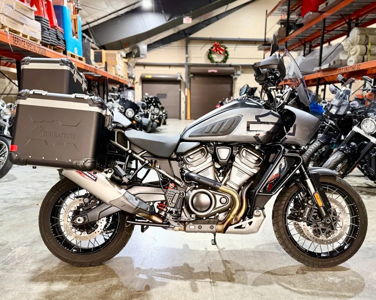 Silver and black adventure motorcycle with Touratech side cases parked indoors among other motorcycles.