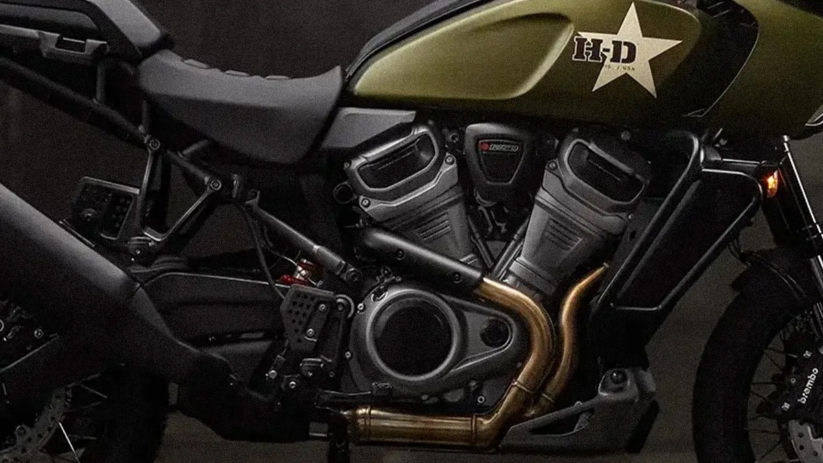 Close-up of a black and olive green Harley-Davidson motorcycle engine with brass exhaust pipes and a star logo on the fuel tank.