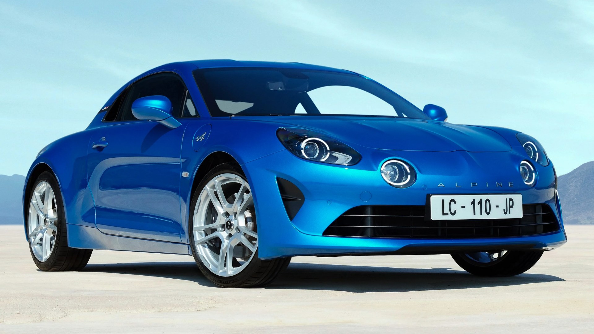Blue Alpine sports car with silver wheels parked on a flat desert surface.