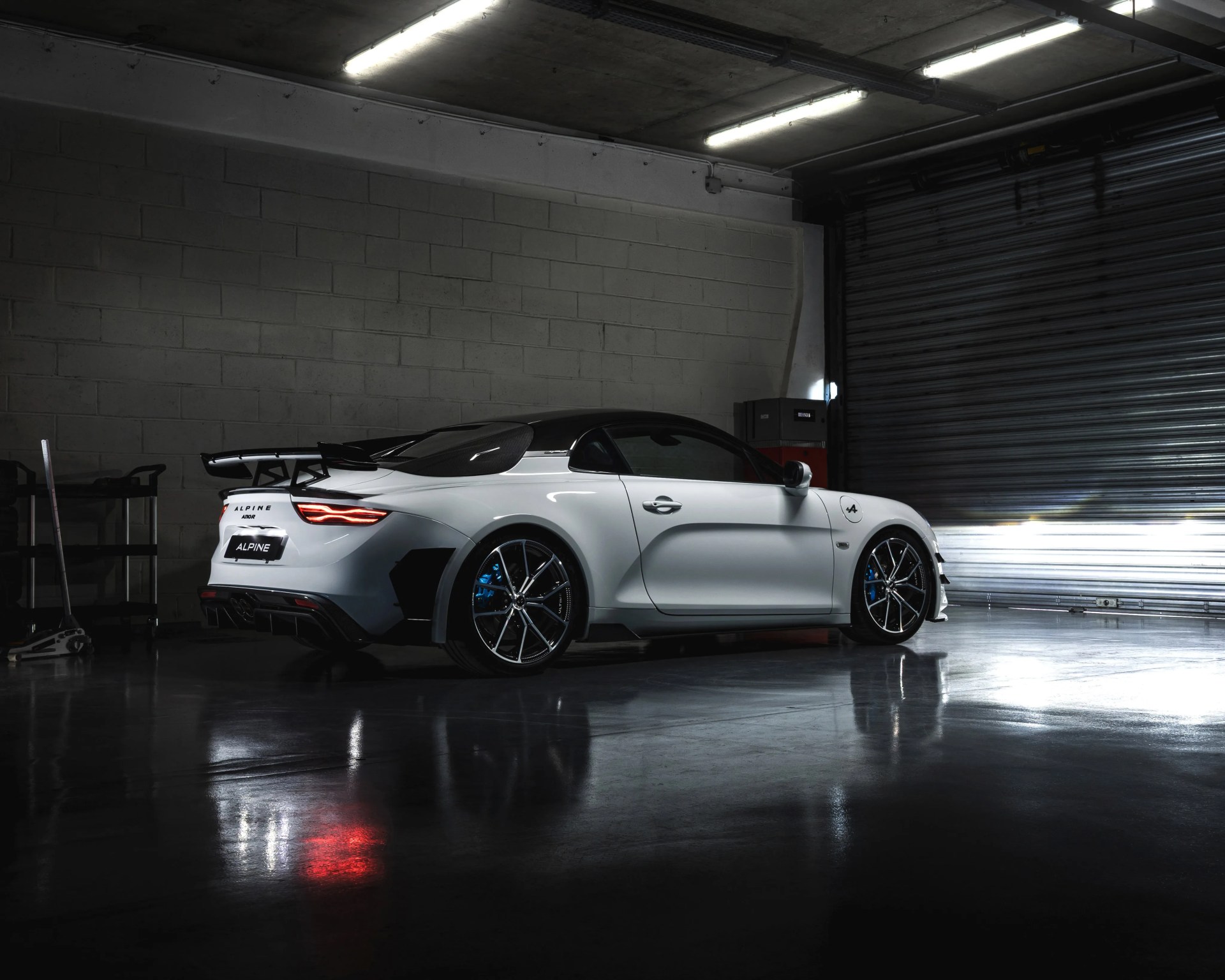 White Alpine A110 sports car with black roof and rear spoiler parked in a dimly lit garage.