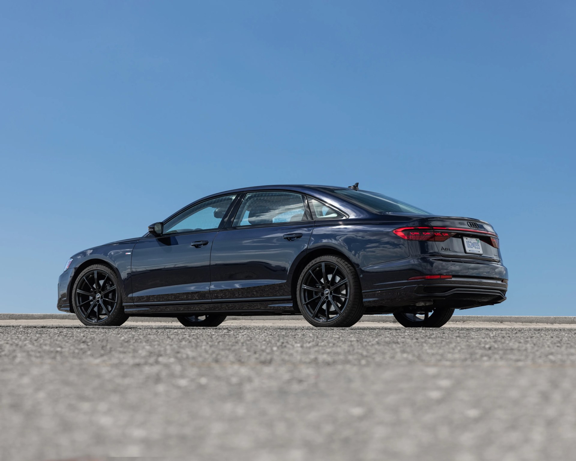 Black Audi A8L sedan with black alloy wheels parked on asphalt under clear blue sky.
