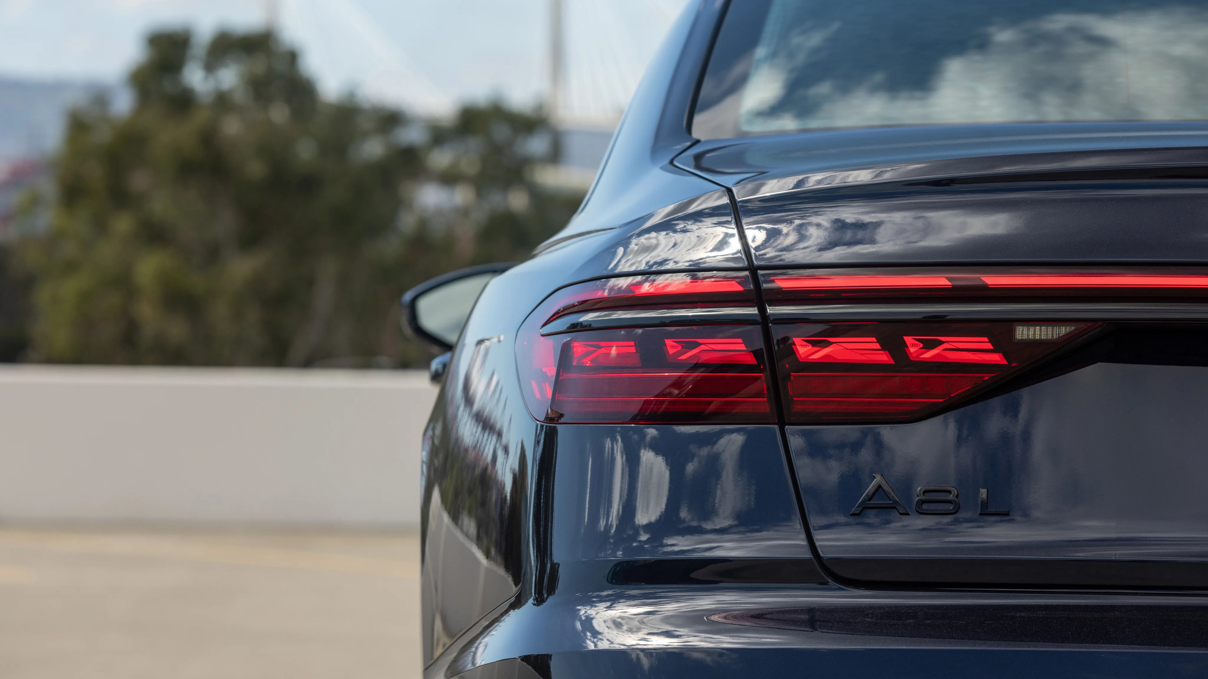 Rear view of a black Audi A8 L showing the left taillight and badge on a blurred outdoor background.