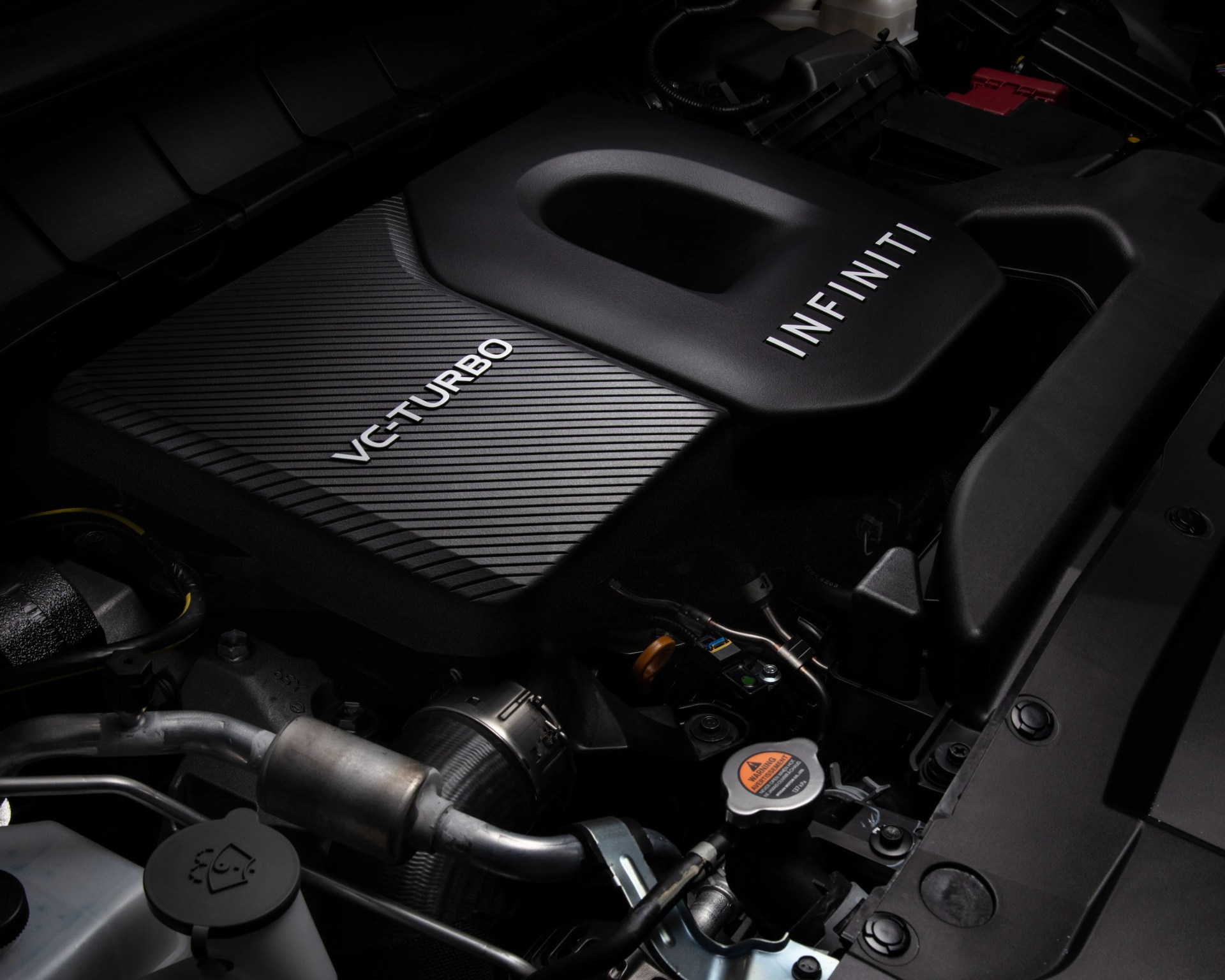 Black engine cover with "VC-TURBO" and "INFINITI" branding inside a car engine bay.