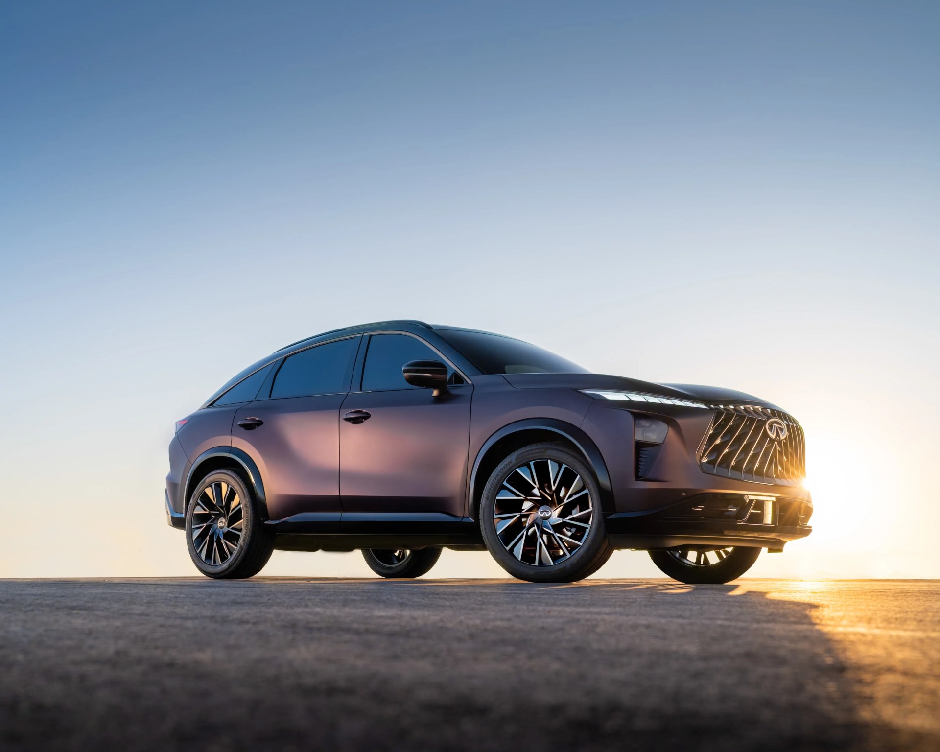 Matte purple Infiniti SUV with large black and silver wheels parked on a flat surface at sunset.