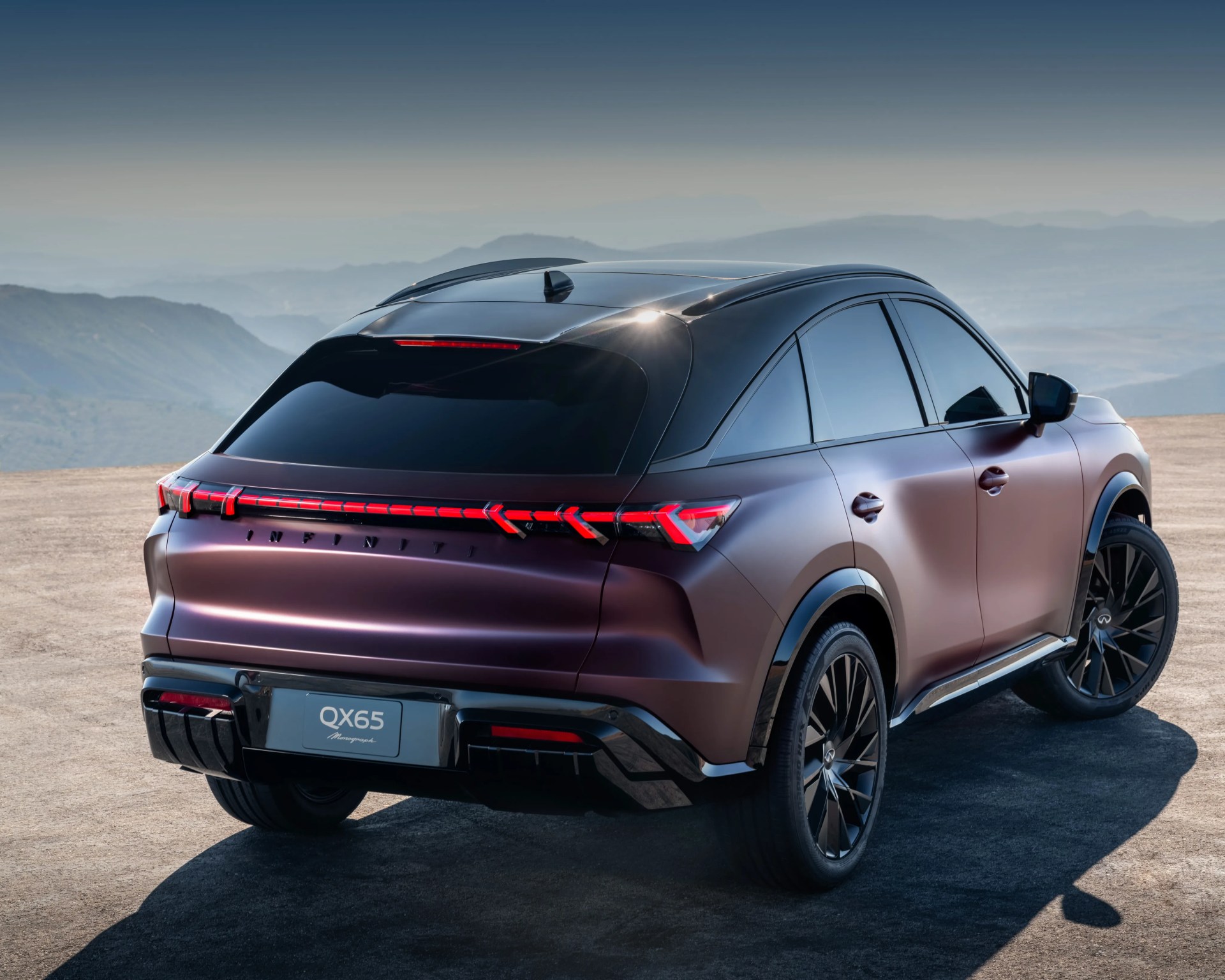 Rear three-quarter view of a matte purple Infiniti QX65 SUV with black roof and tinted windows on a mountain overlook.