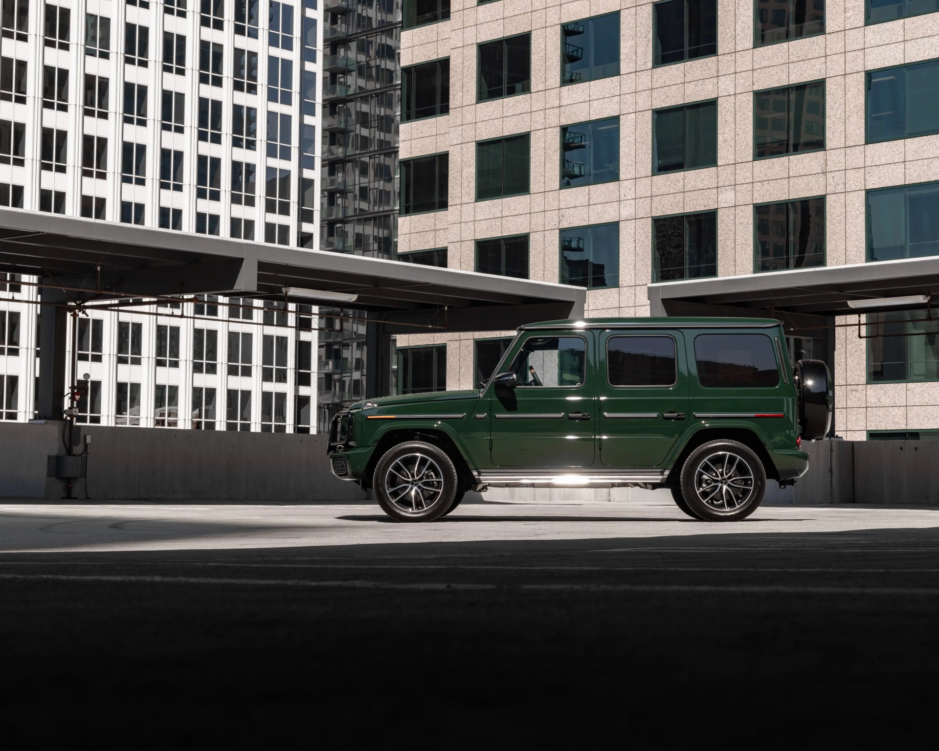 Dark green Mercedes-Benz G-Class SUV parked in an urban setting with modern glass and concrete buildings in the background.