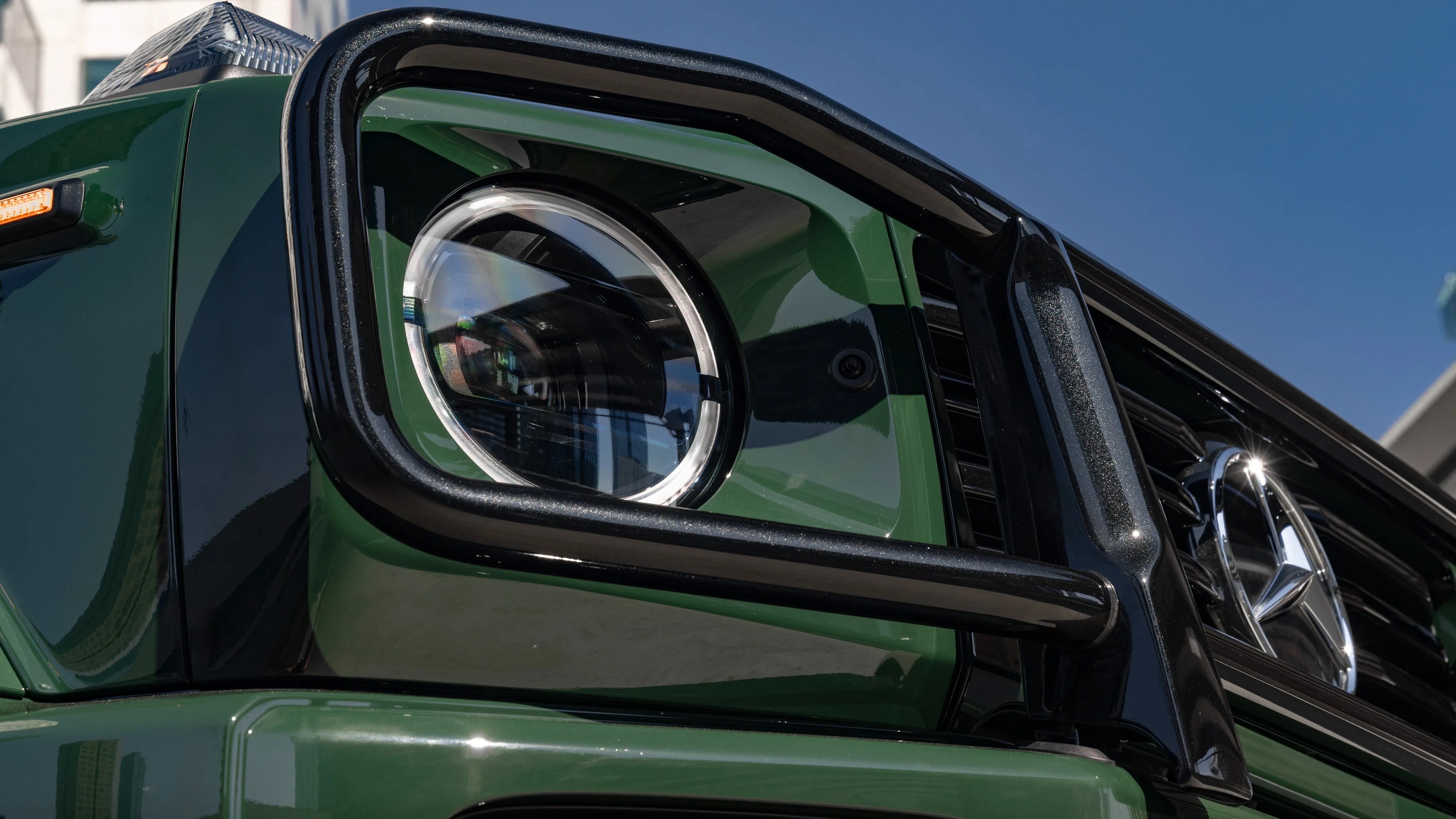 Close-up of a green Mercedes-Benz G-Class headlight with black grille guard and chrome star emblem.