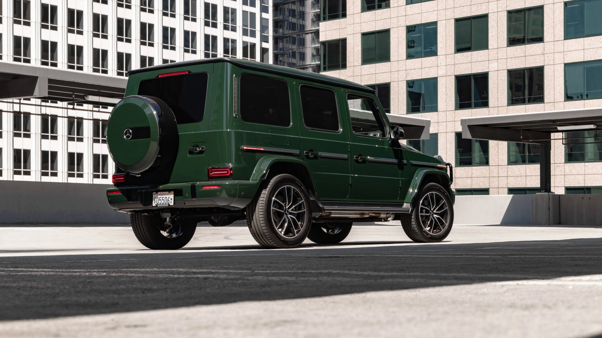 Dark green Mercedes-Benz G-Class SUV parked in an urban setting with modern office buildings in the background.