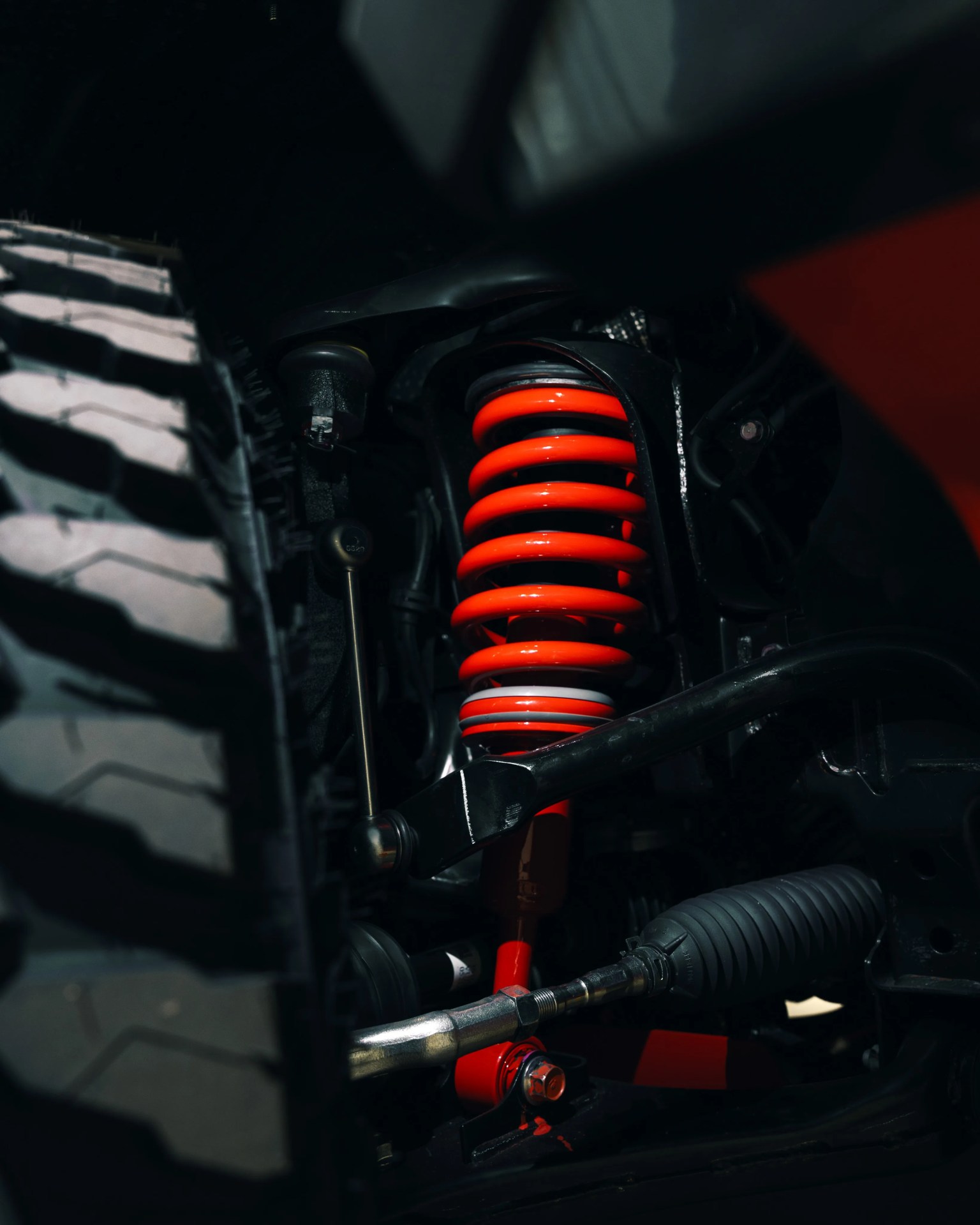 Close-up of a red coil spring suspension system and tire tread on a vehicle.