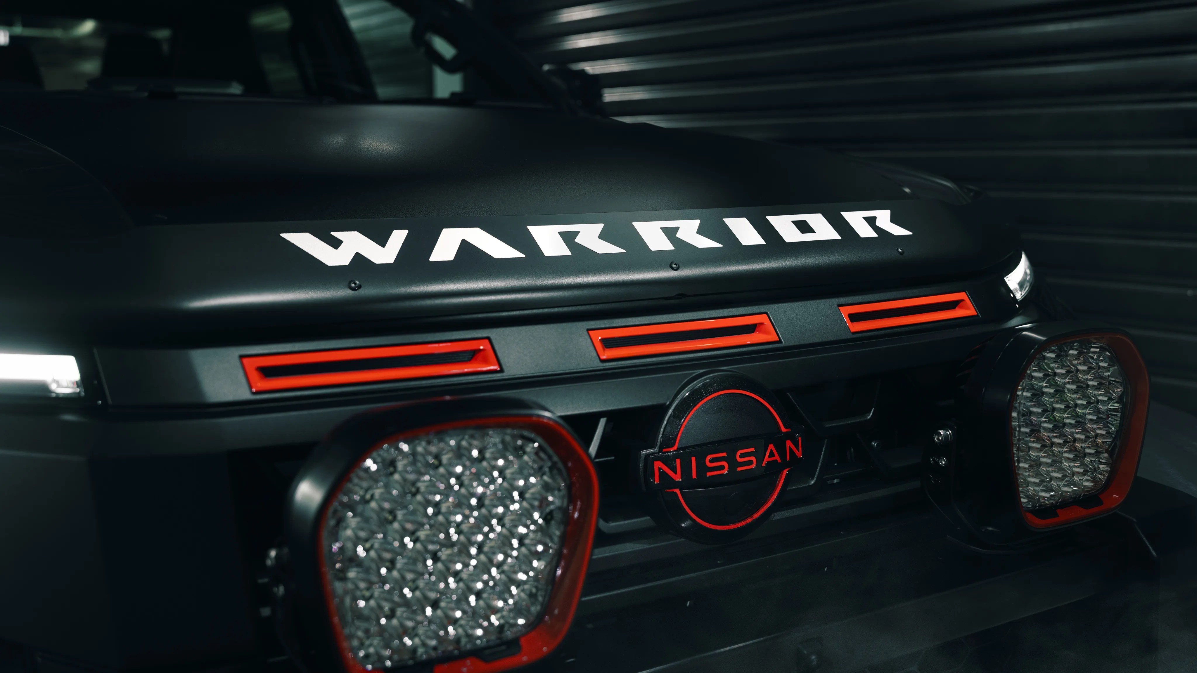 Front grille of a black Nissan Warrior vehicle with red accents and LED lights.