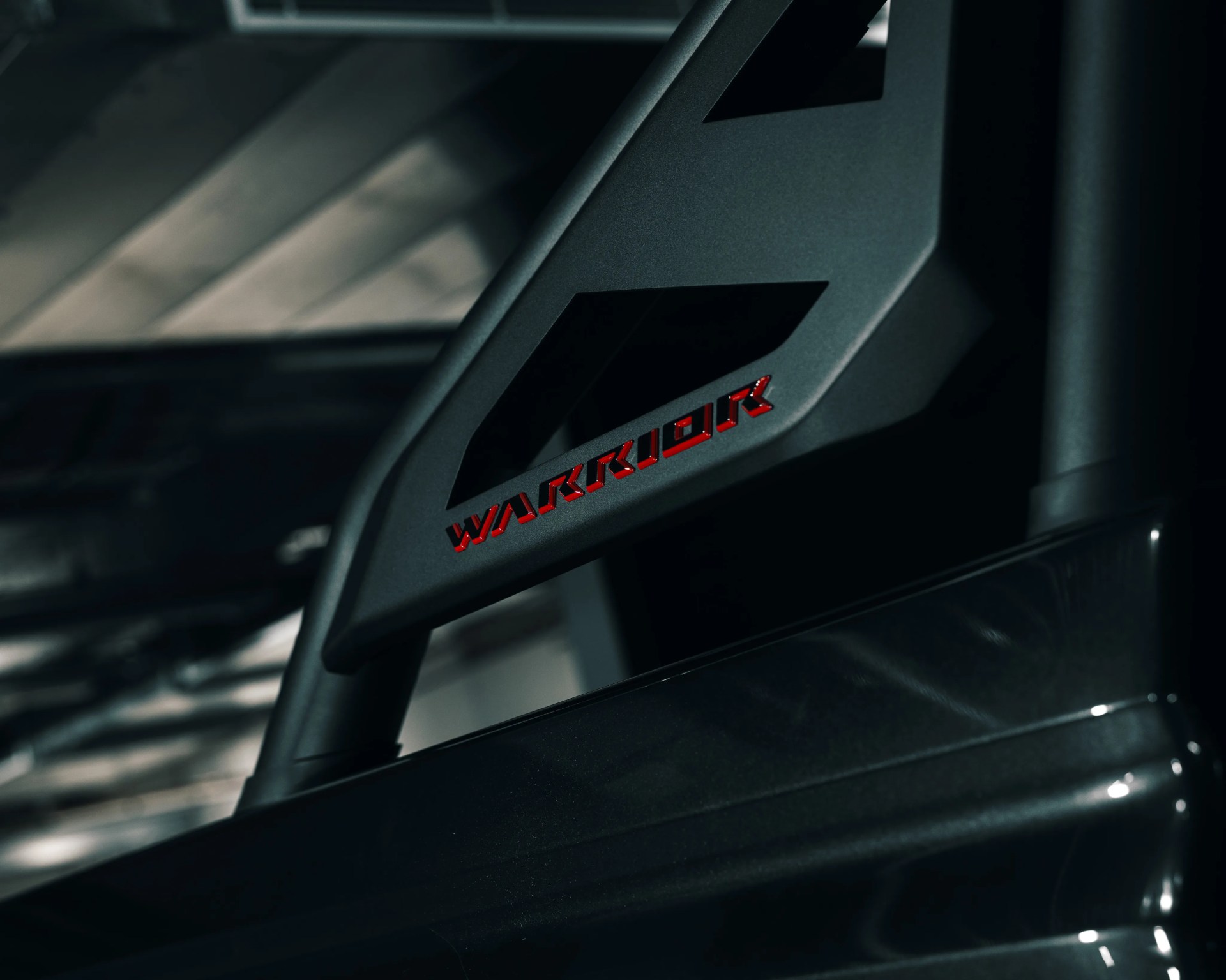 Close-up of a dark metallic vehicle part with red "WARRIOR" lettering.