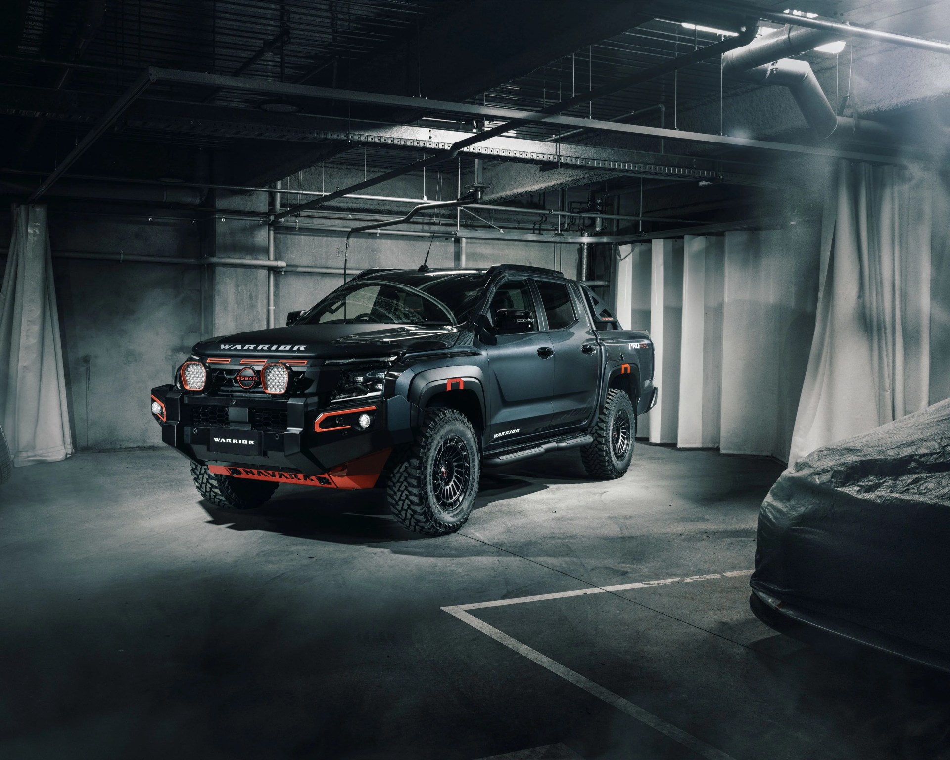 Matte black Nissan Warrior pickup truck with orange accents parked in a dimly lit industrial garage.
