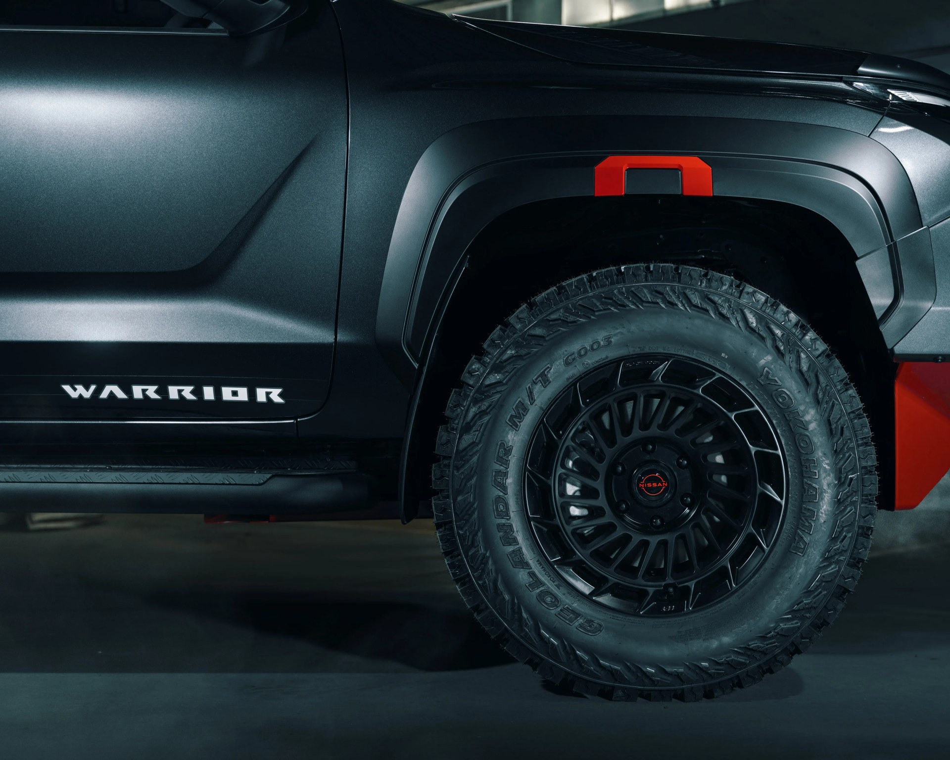 Close-up of black off-road tire with Yokohama branding on a dark gray vehicle with "WARRIOR" text and red accents.