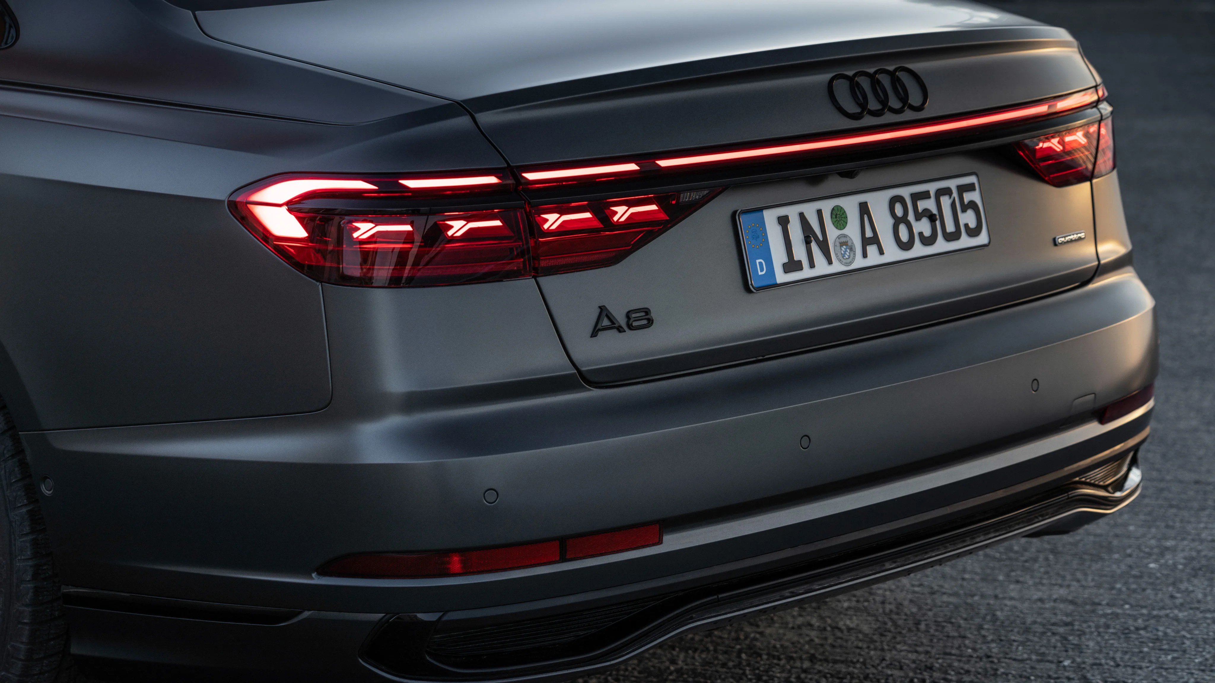 Rear view of a matte gray Audi A8 with illuminated taillights and a European license plate.