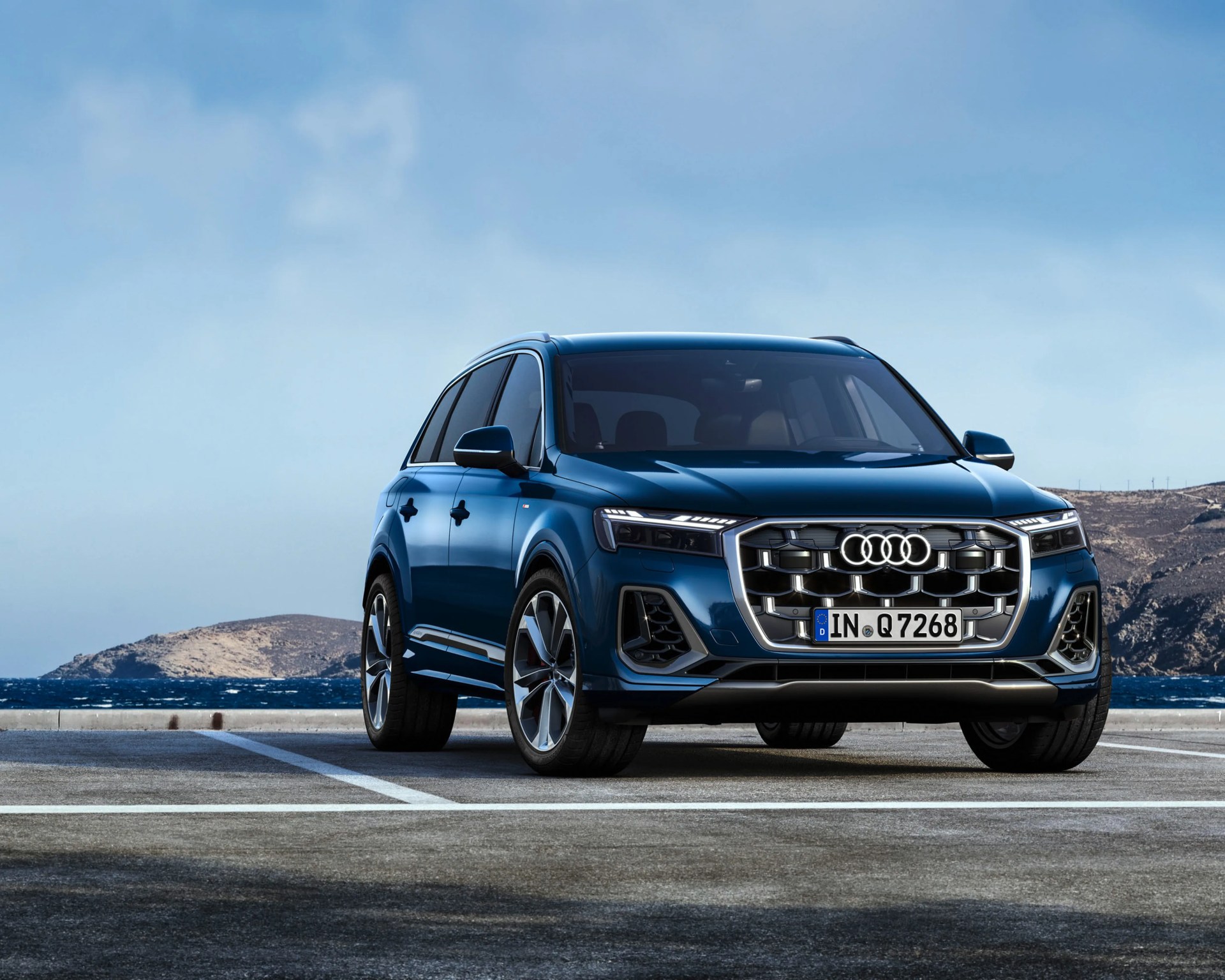 Blue Audi Q7 SUV parked in an outdoor lot with mountains and sea in the background.