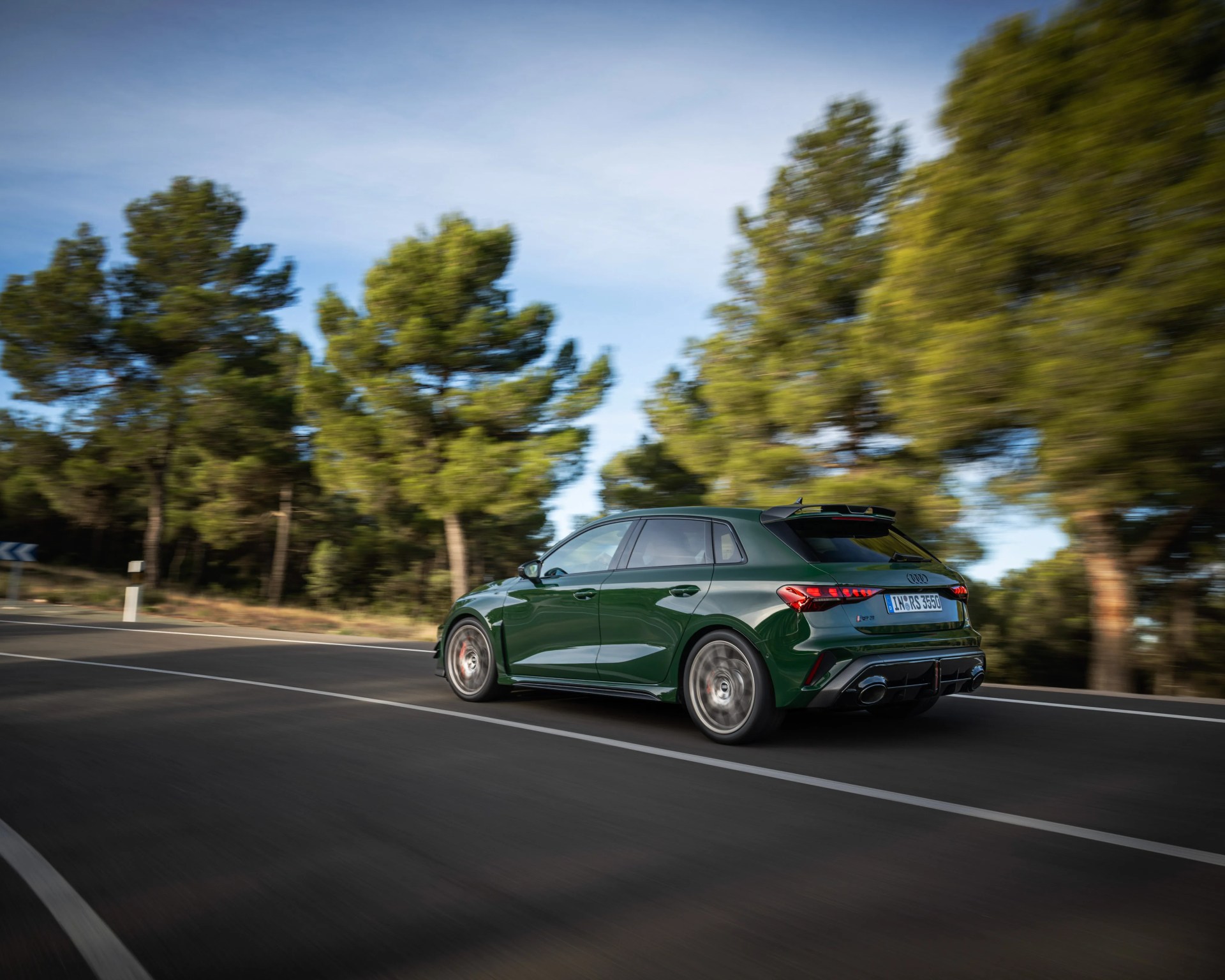 Dark green Audi RS3 Sportback driving on a curved road with blurred trees in the background.