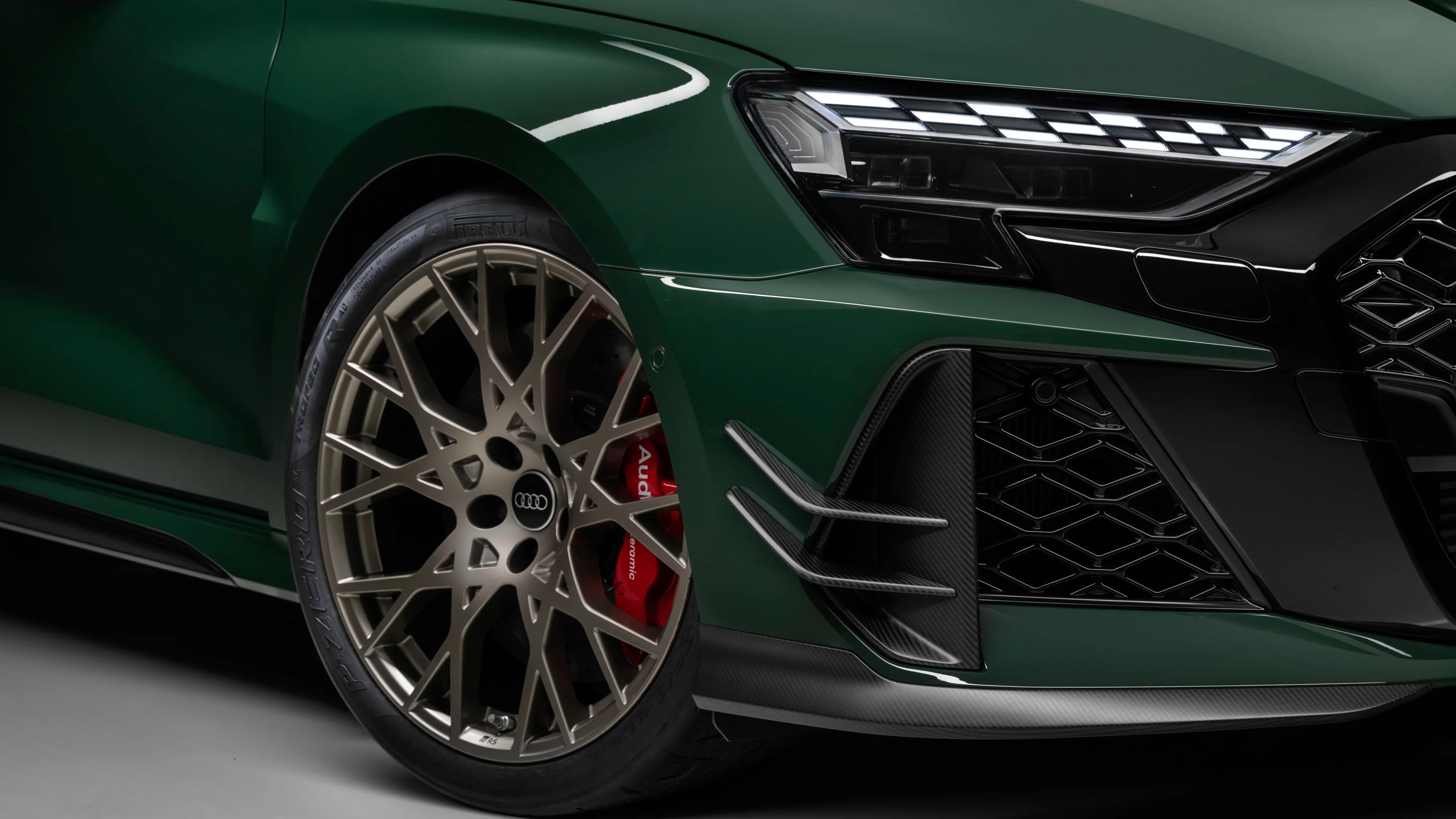 Close-up of a green Audi car's front wheel with bronze multi-spoke rim, red brake caliper, and LED headlight.