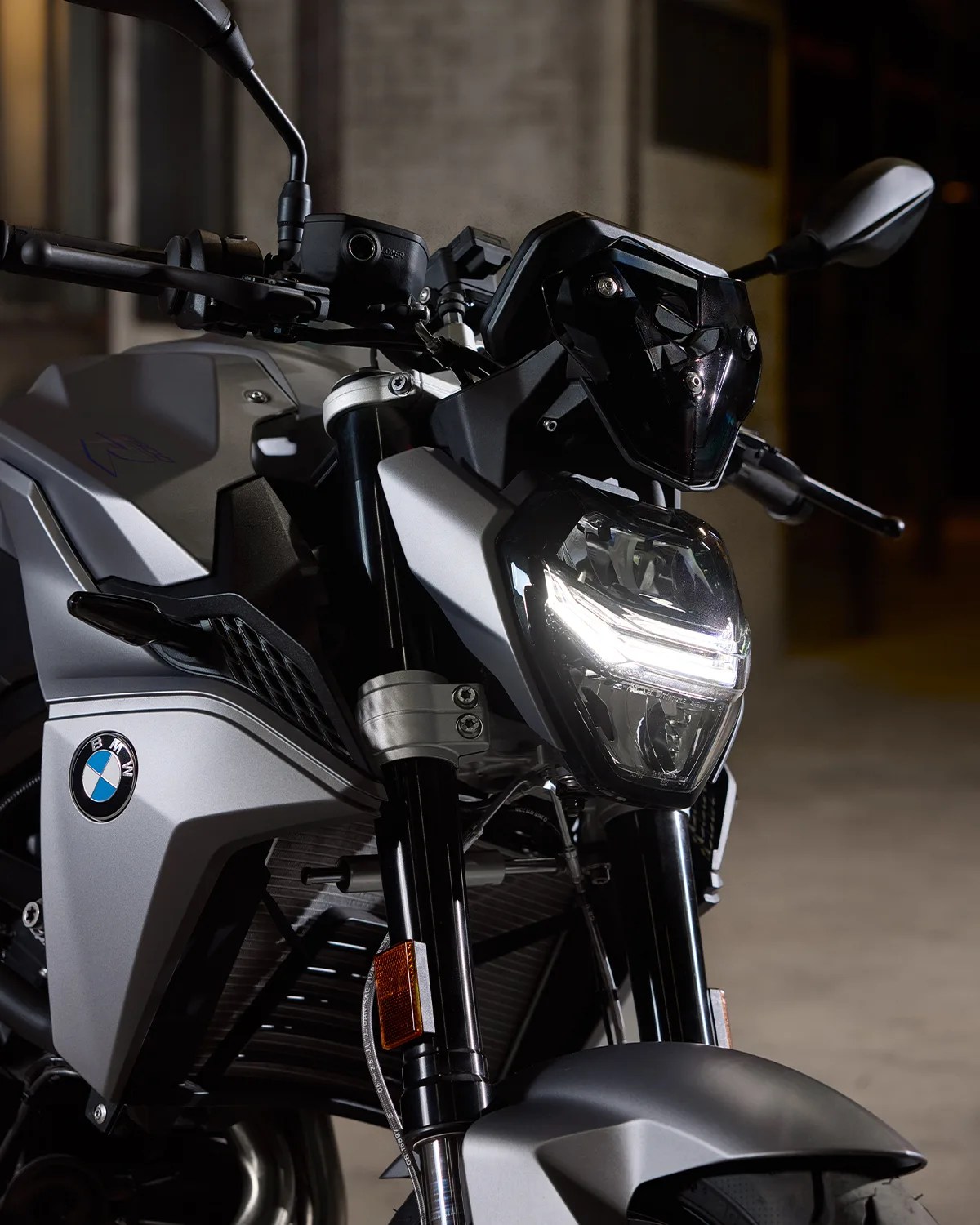 Close-up of a silver BMW motorcycle front with illuminated headlight and black handlebars.