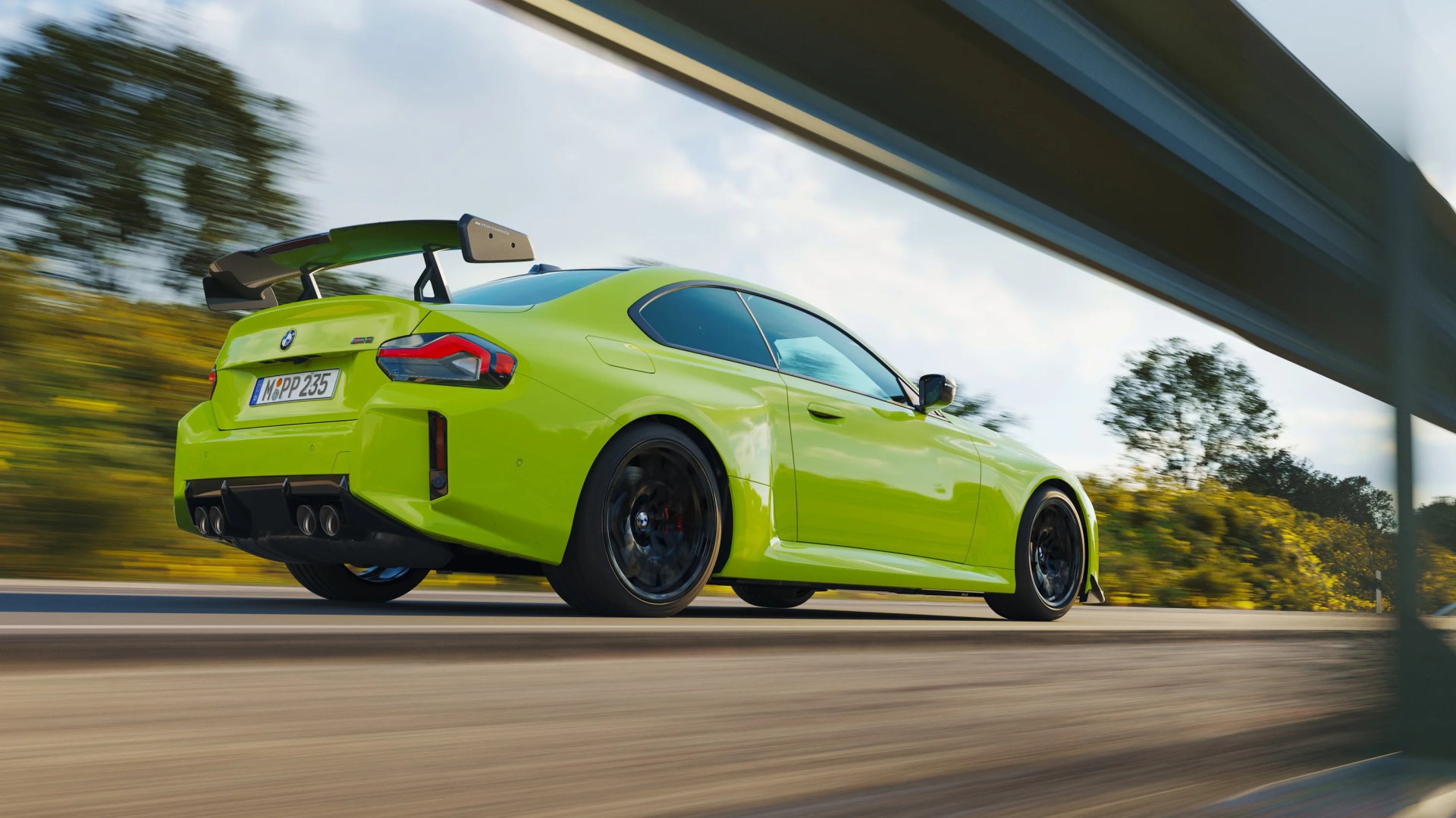 Bright green BMW M2 coupe with black wheels and large rear spoiler driving on a road.