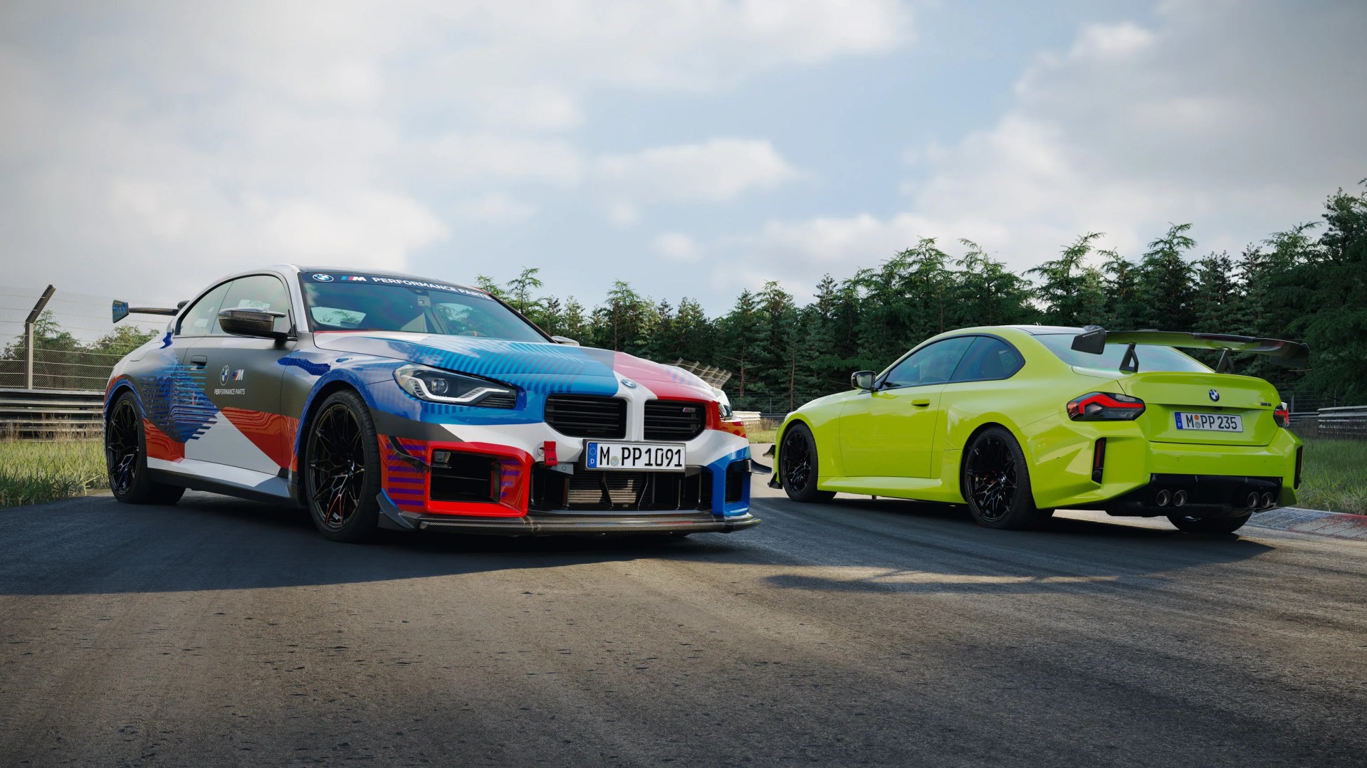 Two BMW M2 cars on a racetrack, one with a multicolor racing livery and the other in bright yellow with a large rear wing.