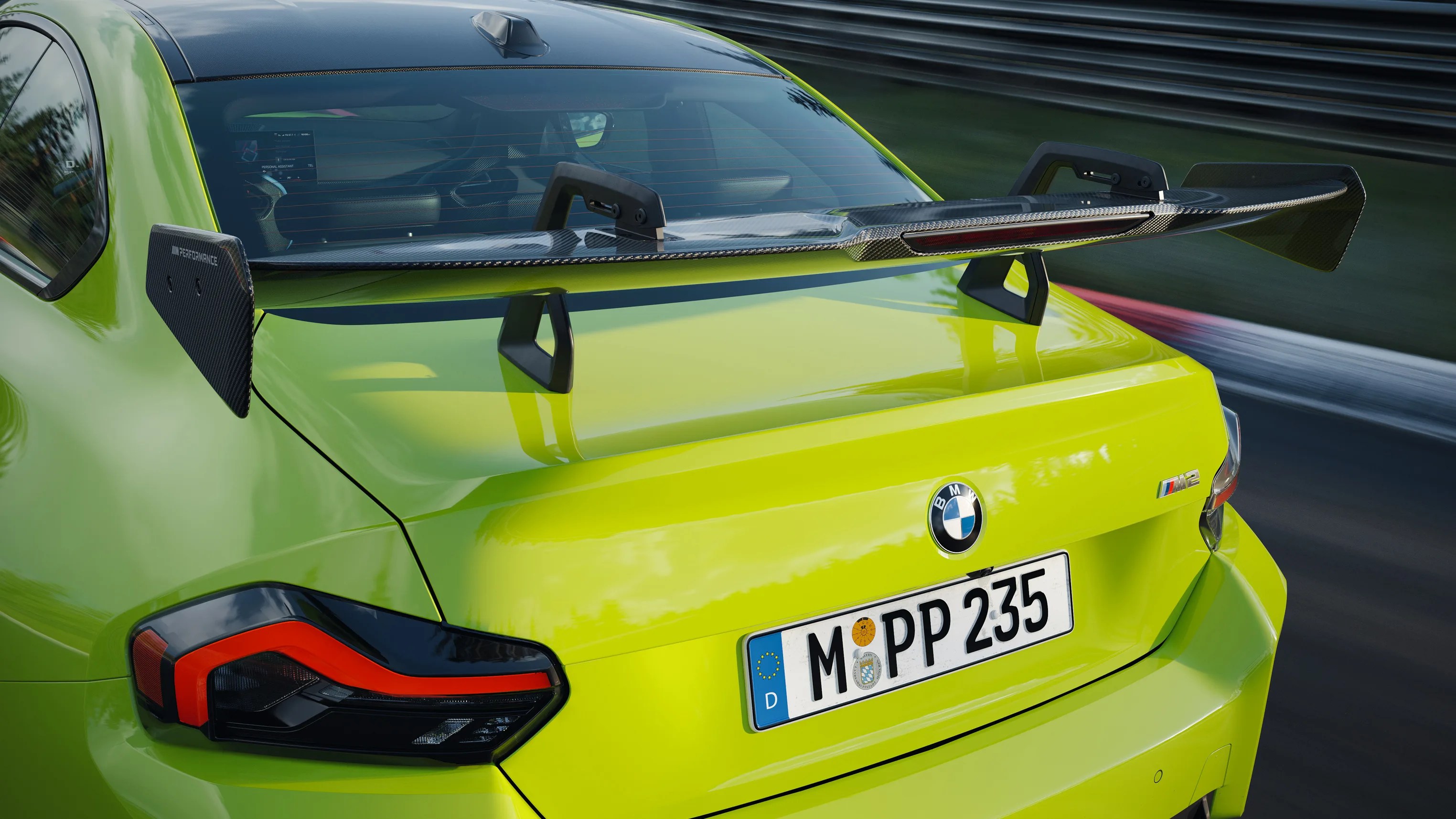 Rear view of a lime green BMW M2 with a large carbon fiber rear wing spoiler on a racetrack.