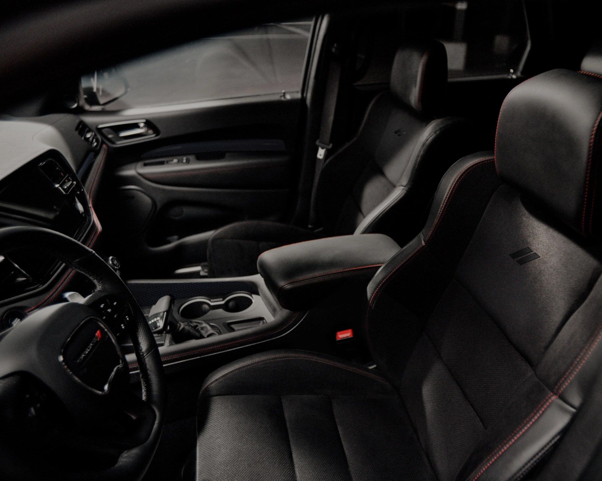 Black leather car seats with red stitching and a center console with cup holders and gear shift.