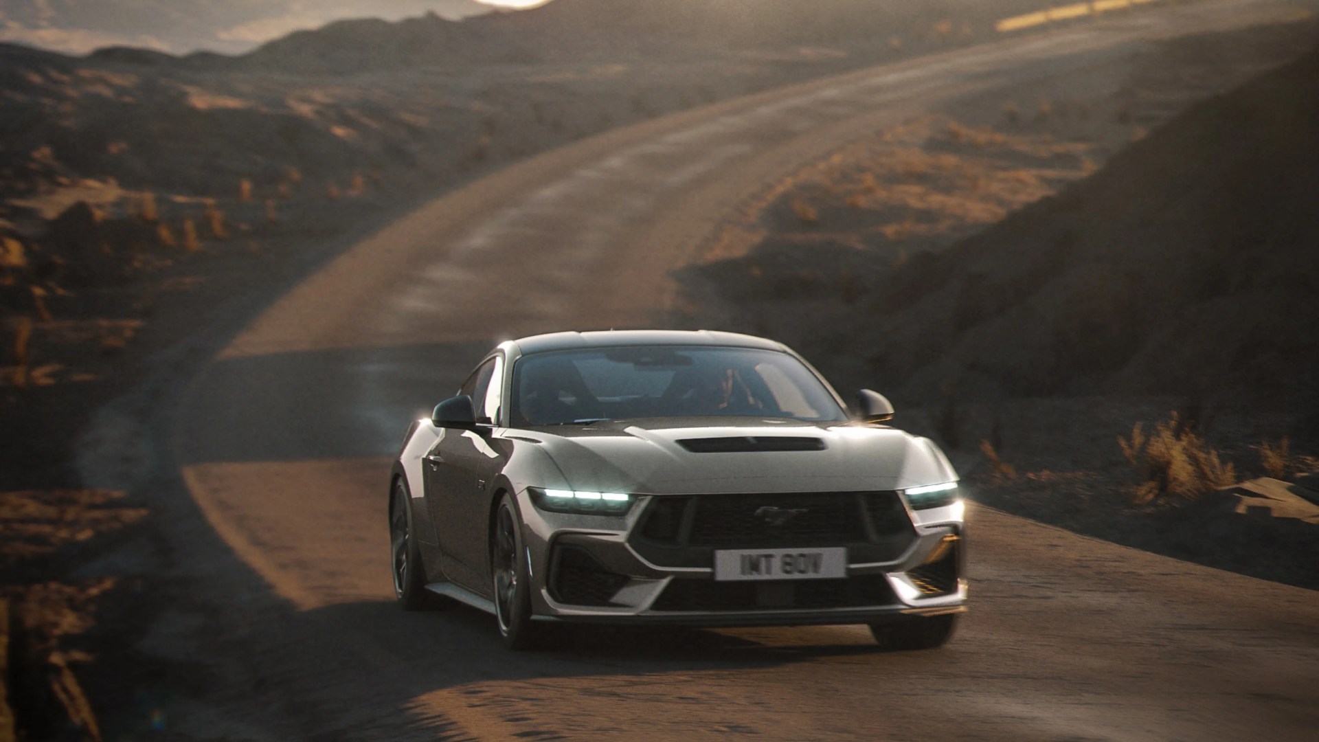Silver Ford Mustang driving on a winding desert road at sunset with headlights on.