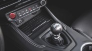 Black leather manual gear shift knob with silver top and white stitching in a car interior.