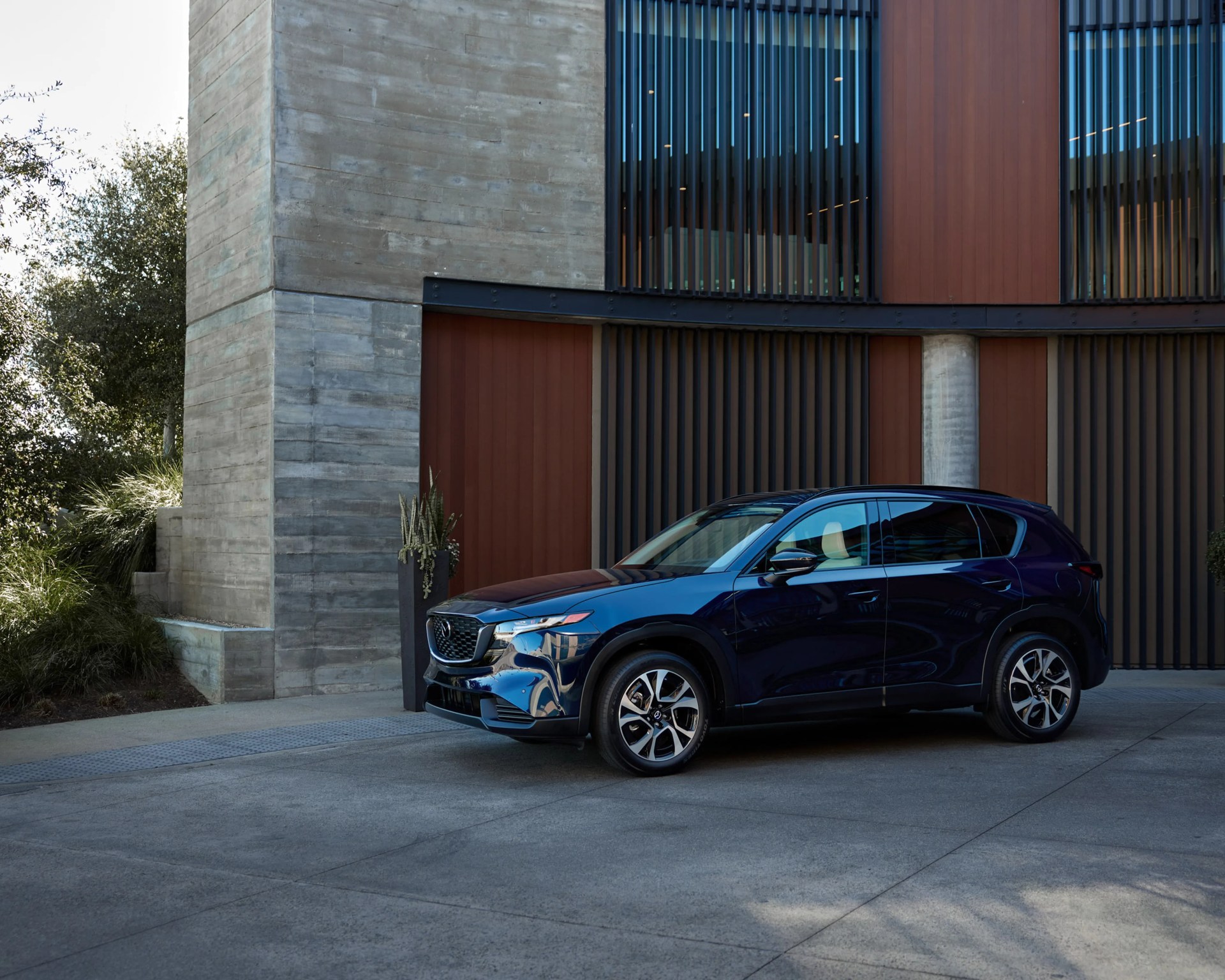 Dark blue Mazda CX-50 SUV parked on a concrete driveway in front of a modern building with wood and concrete facade.