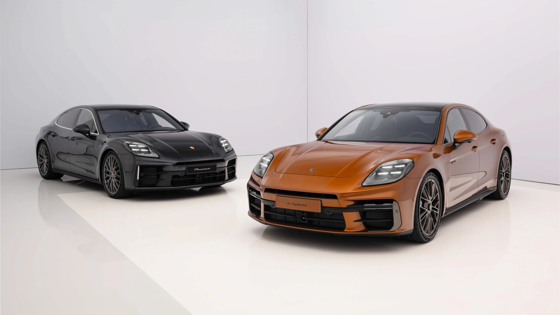 Two Porsche Panamera sedans, one black and one metallic orange, parked in a white studio.