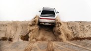Silver Rivian pickup truck kicking up sand while driving off a sandy hill.